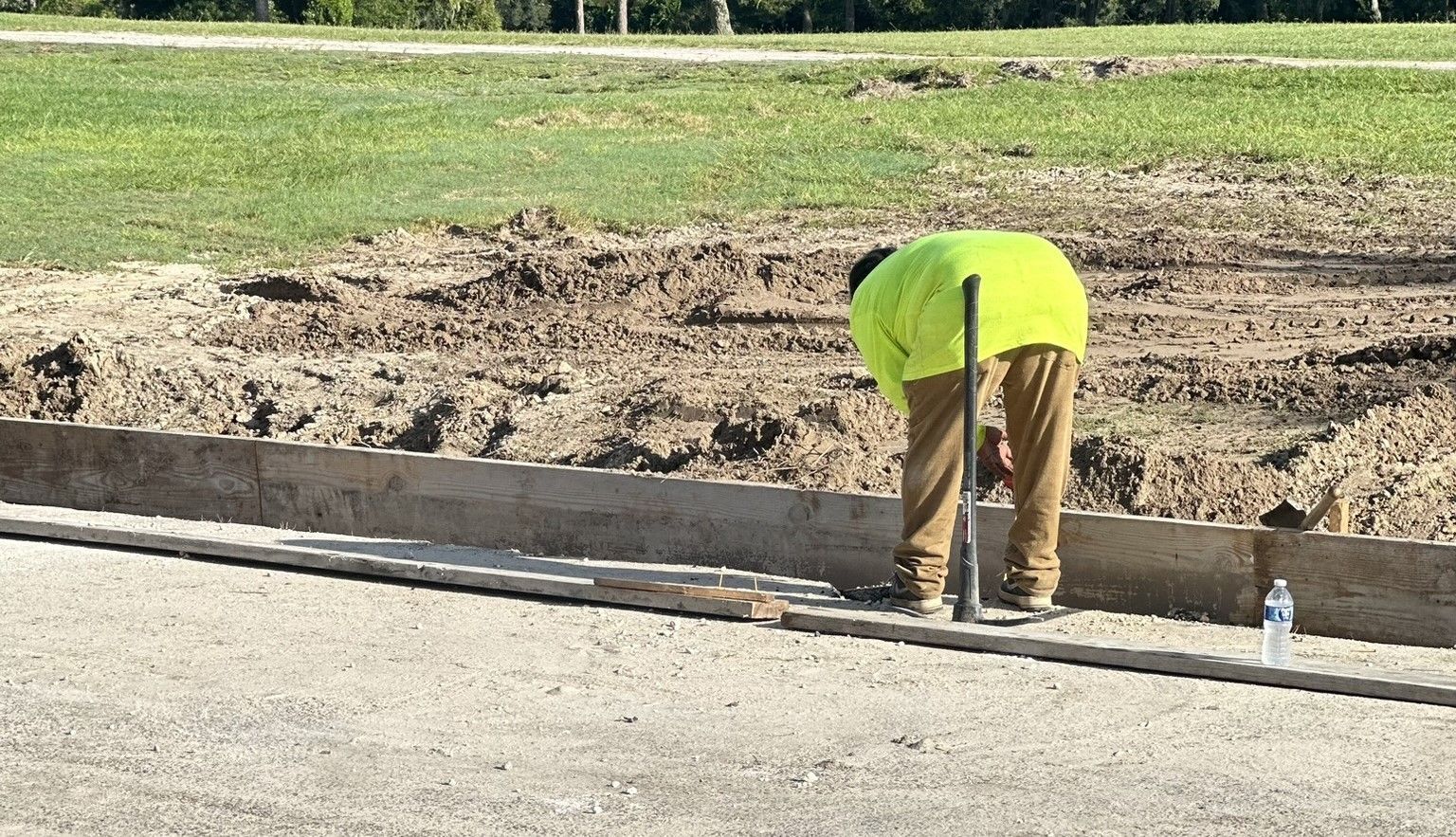 A concrete finisher in a yellow jacket is working on a sidewalk.