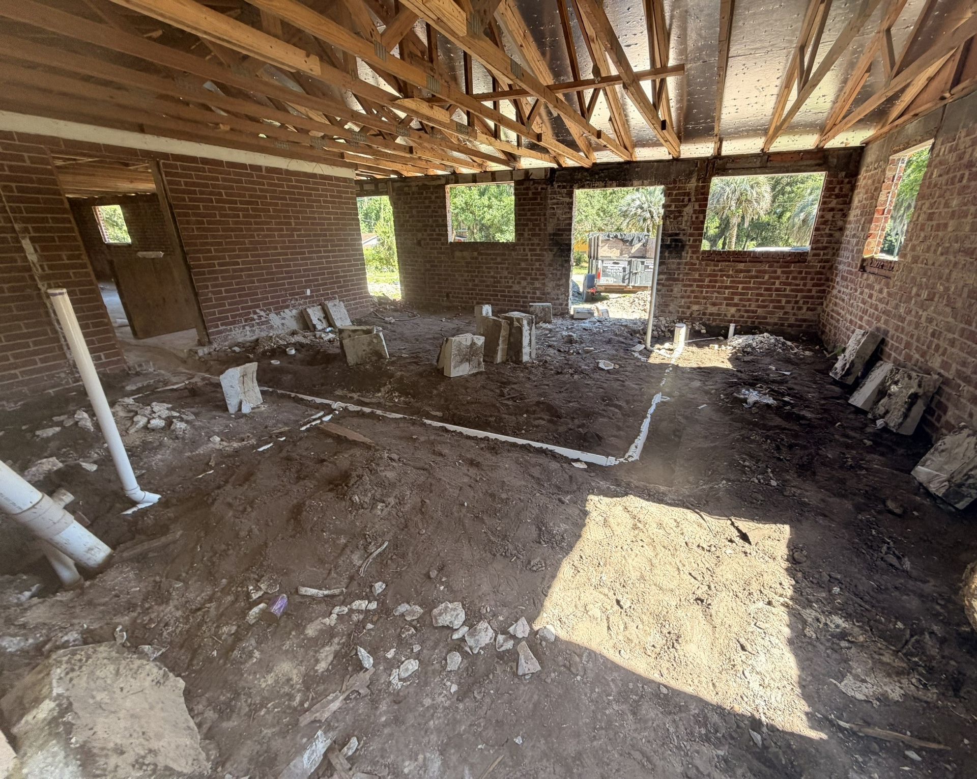 Partially built brick room with exposed ceiling beams, dirt floor, and construction debris in sunlight
