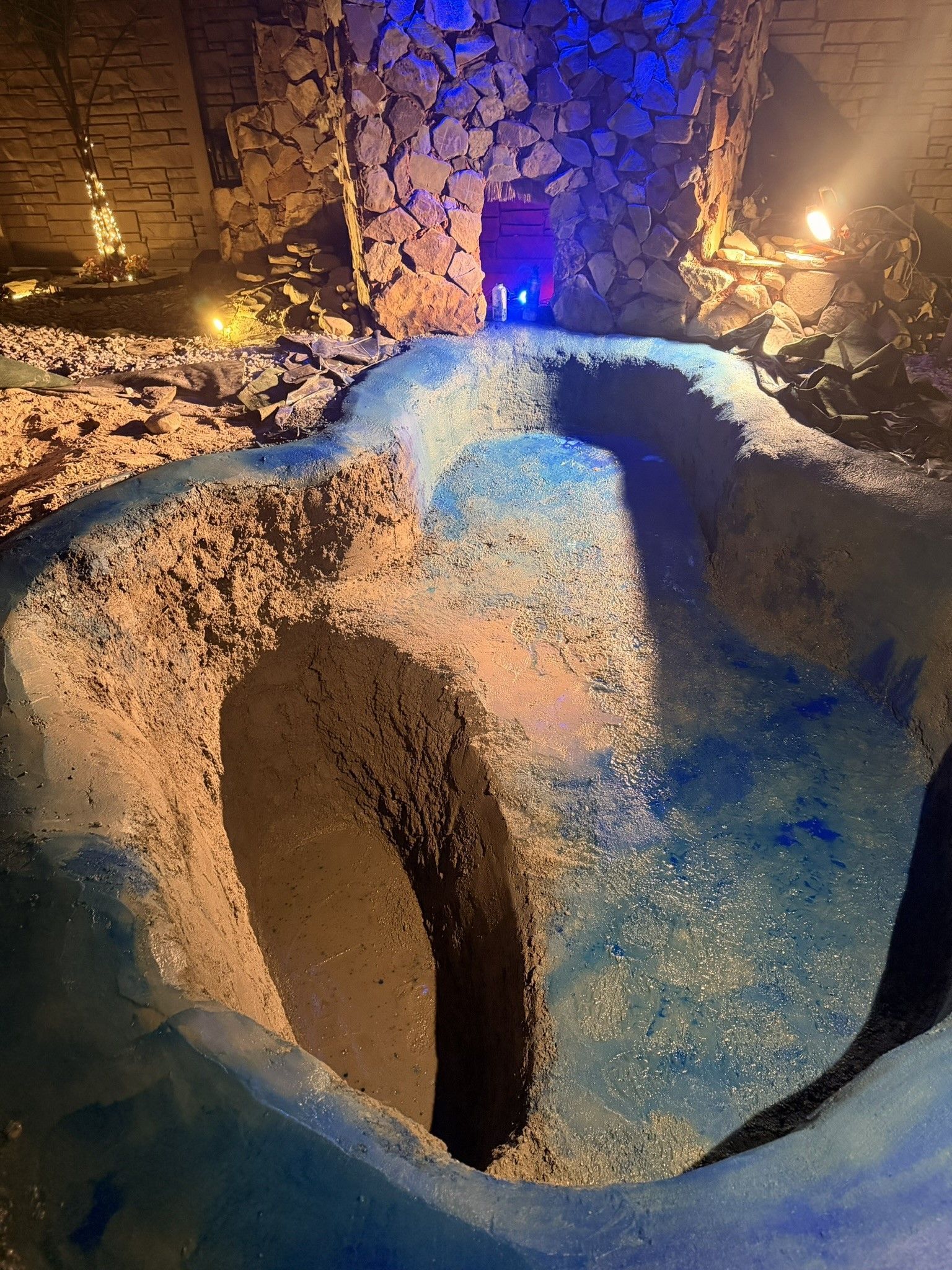 Blue-tiled empty swimming pool with an irregular shape and a stone wall in the background