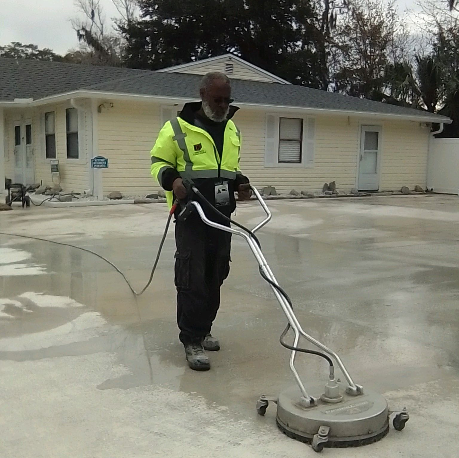 Worker in neon safety vest using a surface cleaner to clean concrete driveway outside an office