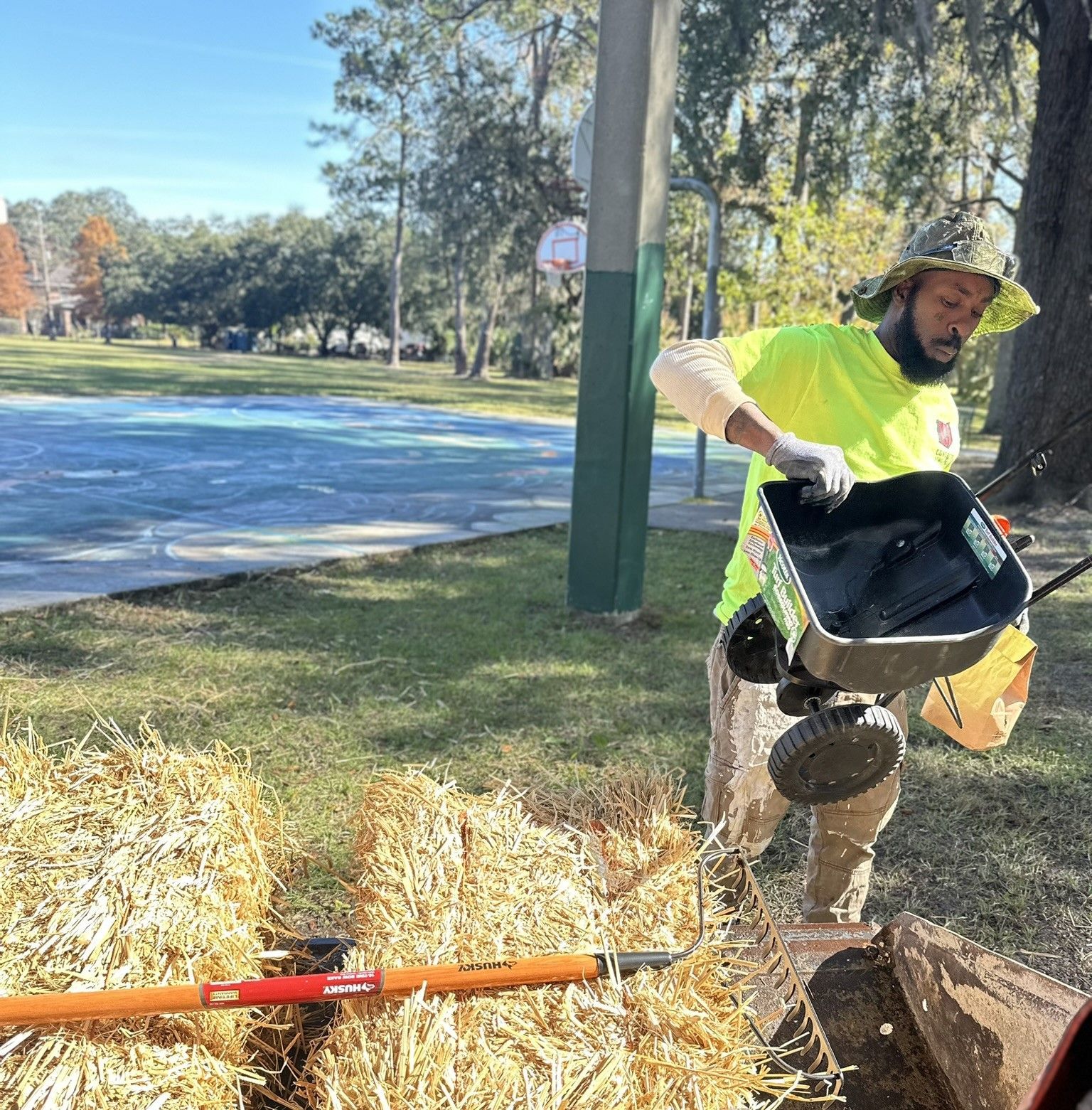 A man in a yellow shirt is pushing a wheelbarrow full of hay bales on a construction site