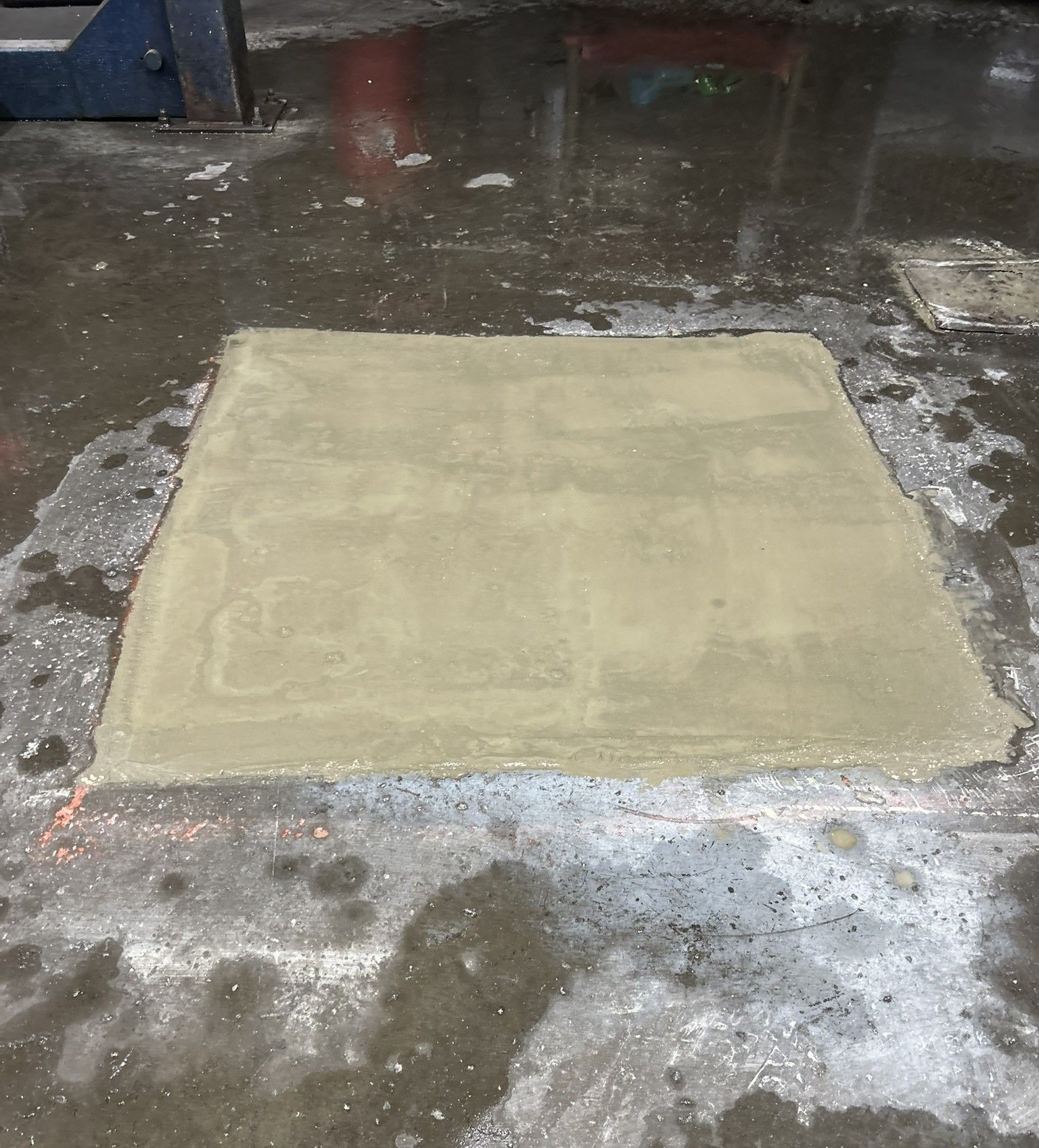 Square concrete patch on a wet, dirty floor in an indoor industrial space