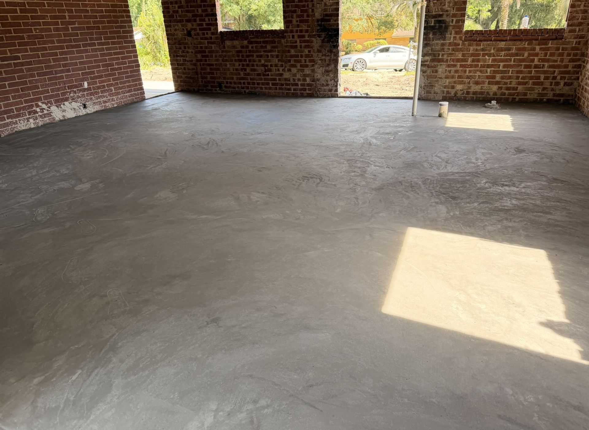 Empty unfinished brick room with a smooth concrete floor and sunlight streaming through window openings.