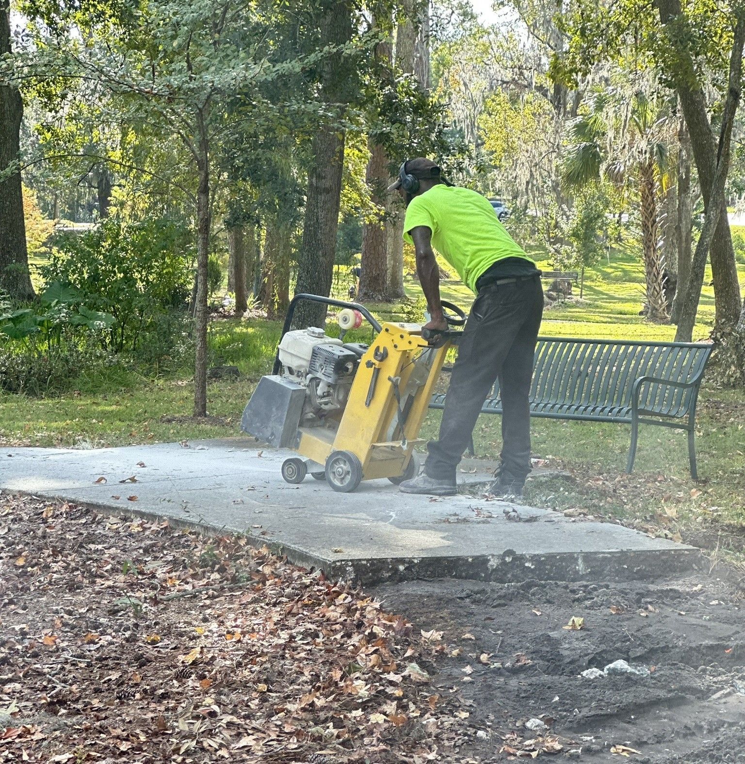 Worker using a yellow concrete saw to cut a slab in a wooded park area