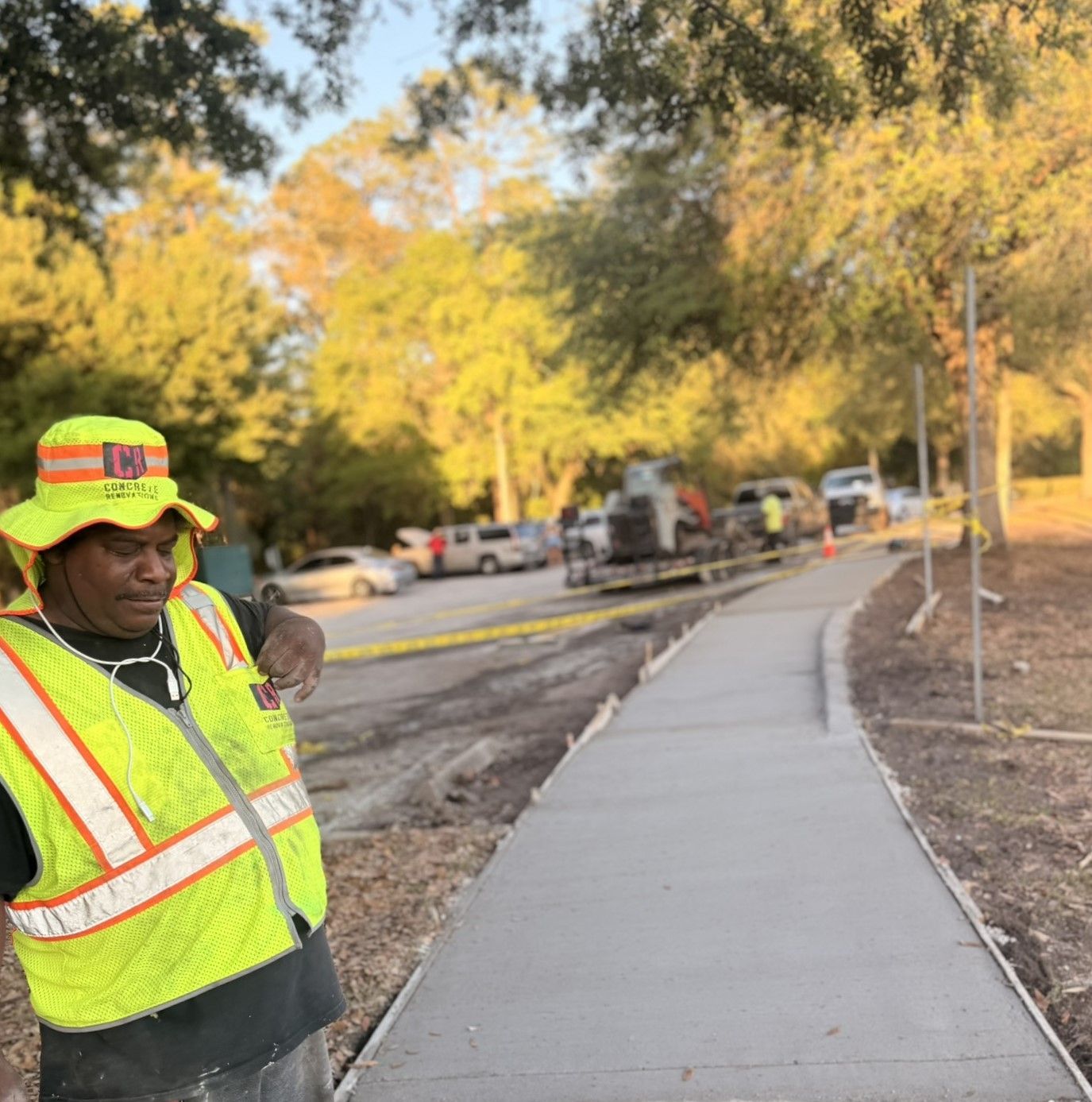 Construction worker in neon safety vest beside a new sidewalk on a tree-lined street