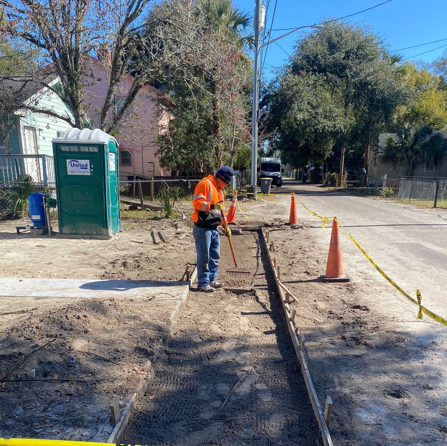 A man is digging in the dirt to pour a concrete sidewalk near a green portable toilet