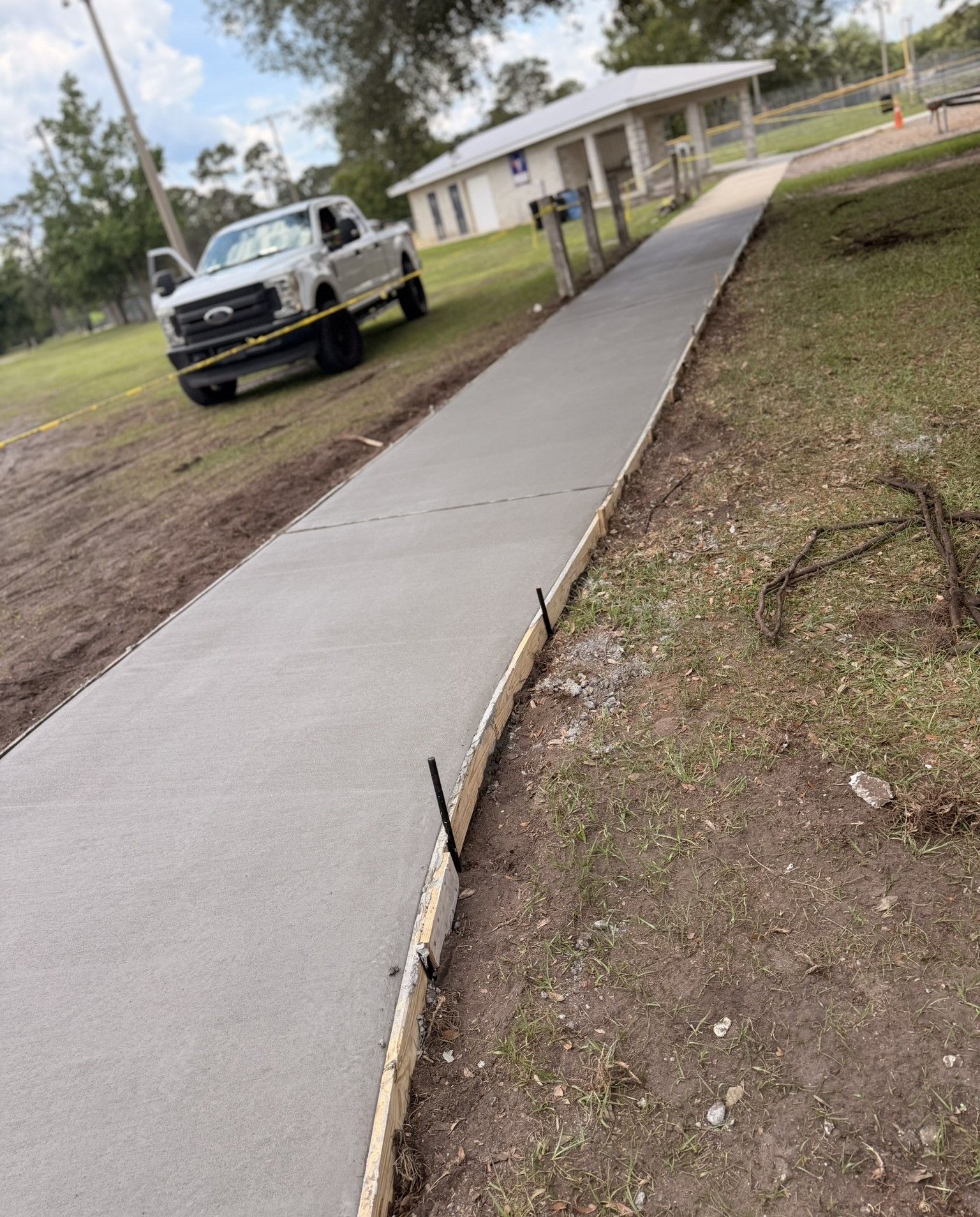 New concrete sidewalk beside a grassy yard with a parked truck and house in the background