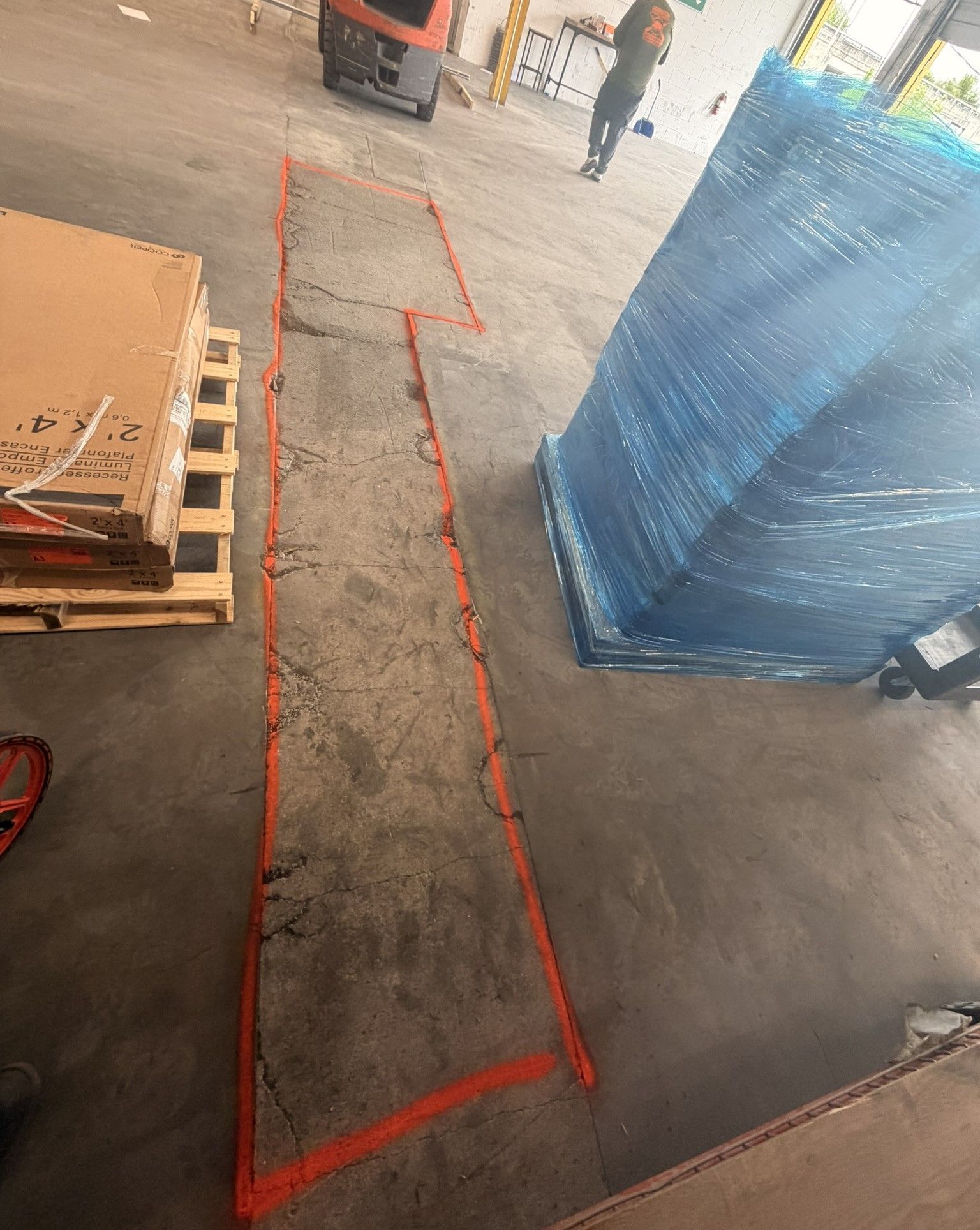 Warehouse aisle with red taped floor markings beside a blue-wrapped pallet and stacked pallets on the left
