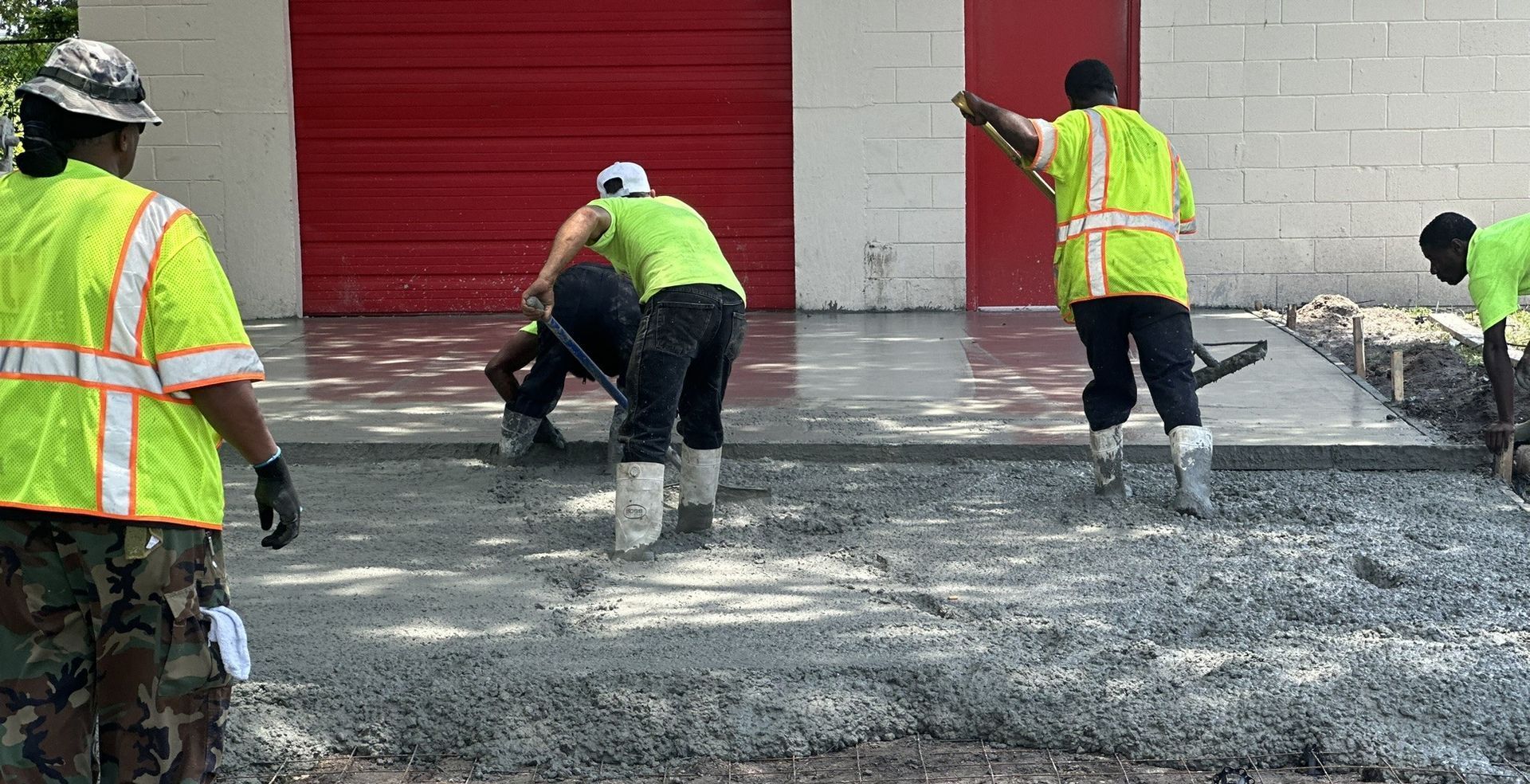 Workers in neon vests spreading wet concrete outside a red garage door