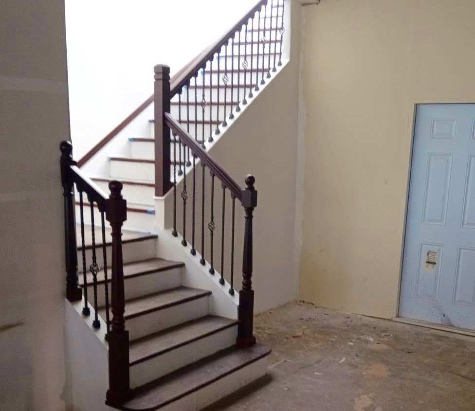 Staircase remodel with dark wooden railings in a bare interior room, beside a light blue door.
