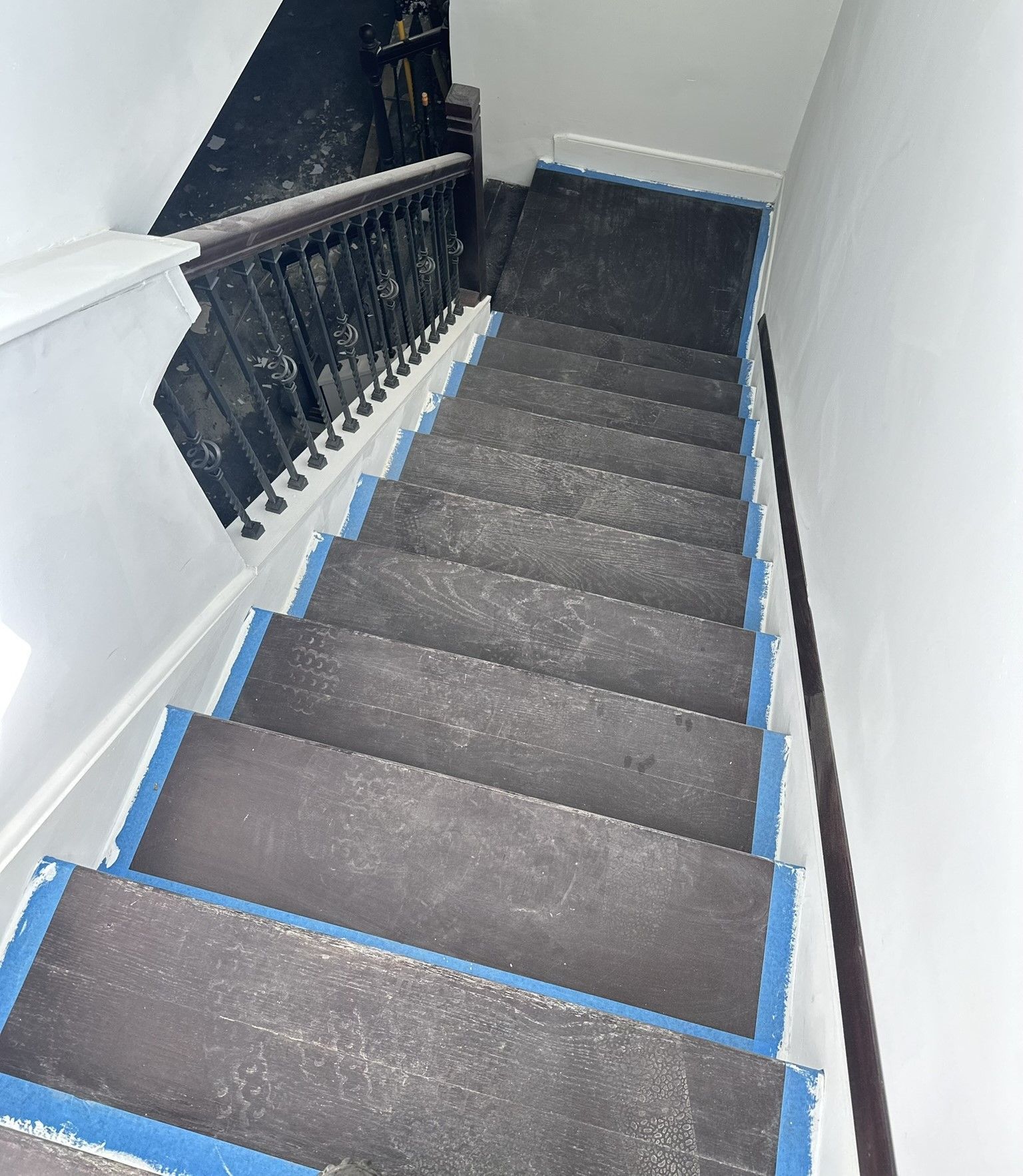 Narrow indoor staircase with dark carpeted steps, black railing, and white walls viewed from above midway through remodel