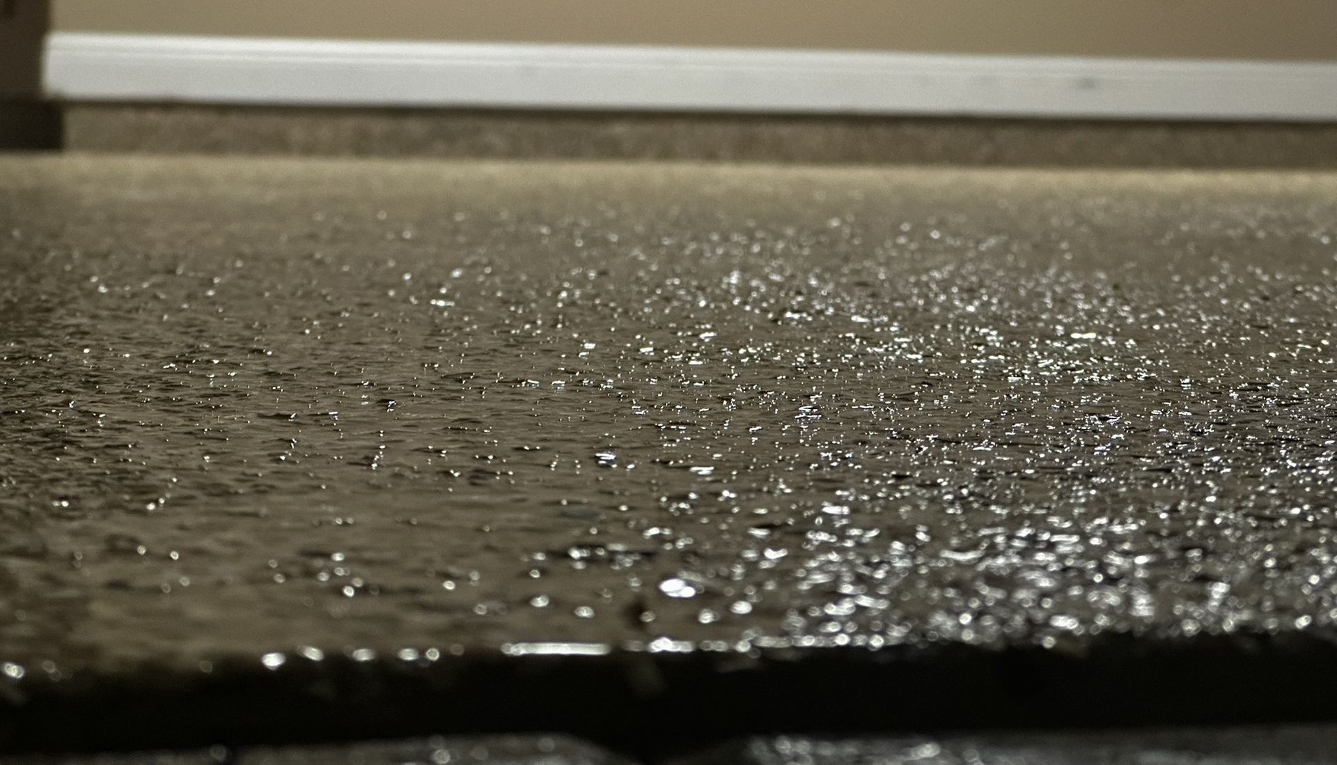 Close-up of wet pavement with glistening water droplets under low light