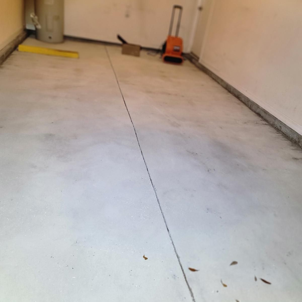 clean garage floor with a central crack, a yellow tool on the left, and an orange jack near the back wall.