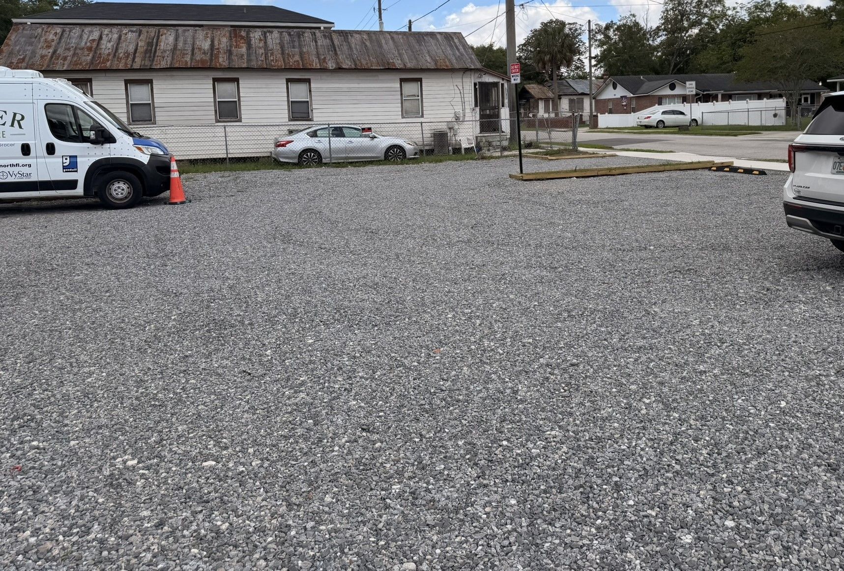 Gravel lot with parked cars beside a low building under an overcast sky