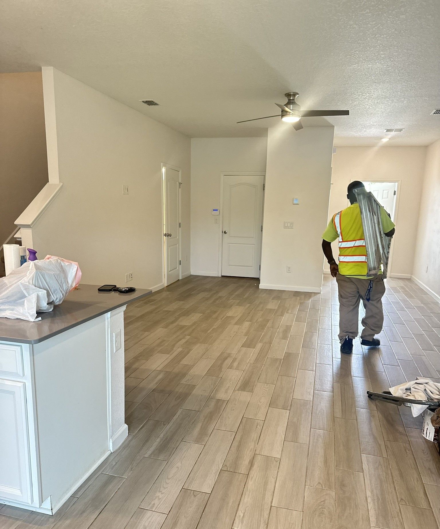 Worker in a yellow safety vest standing in a open concept remodel with wood floors and white walls.
