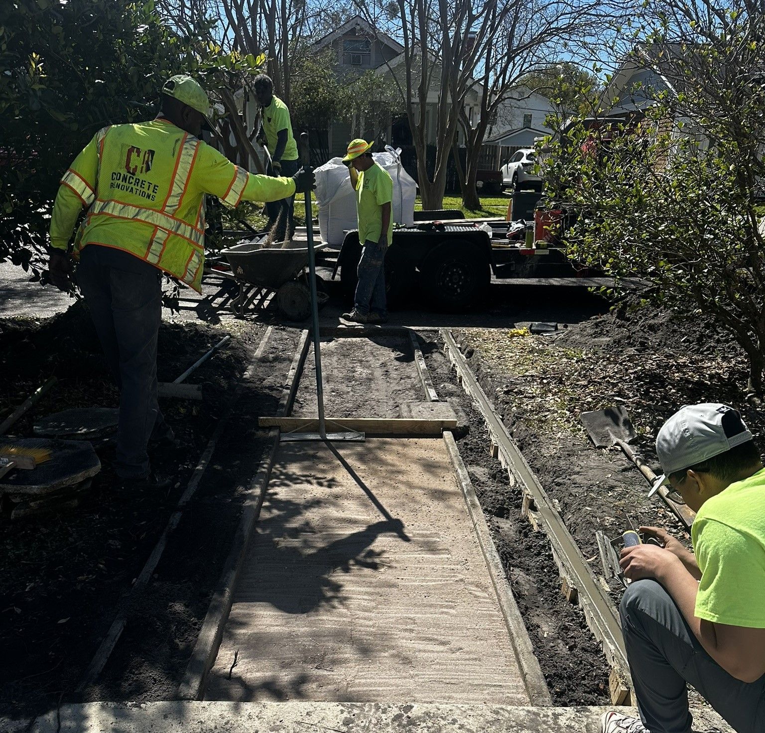 Concrete Renovations workers installing a paver walkway, wearing neon yellow safety vests and hard hats.
