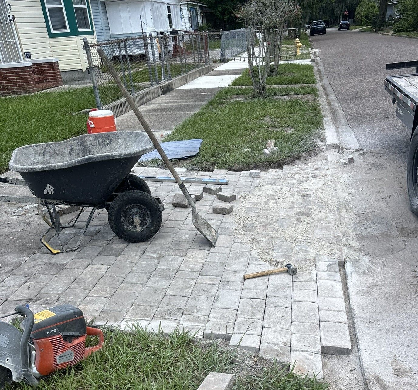 Paver Installation with wheelbarrow, paver bricks, and saw on a sidewalk.