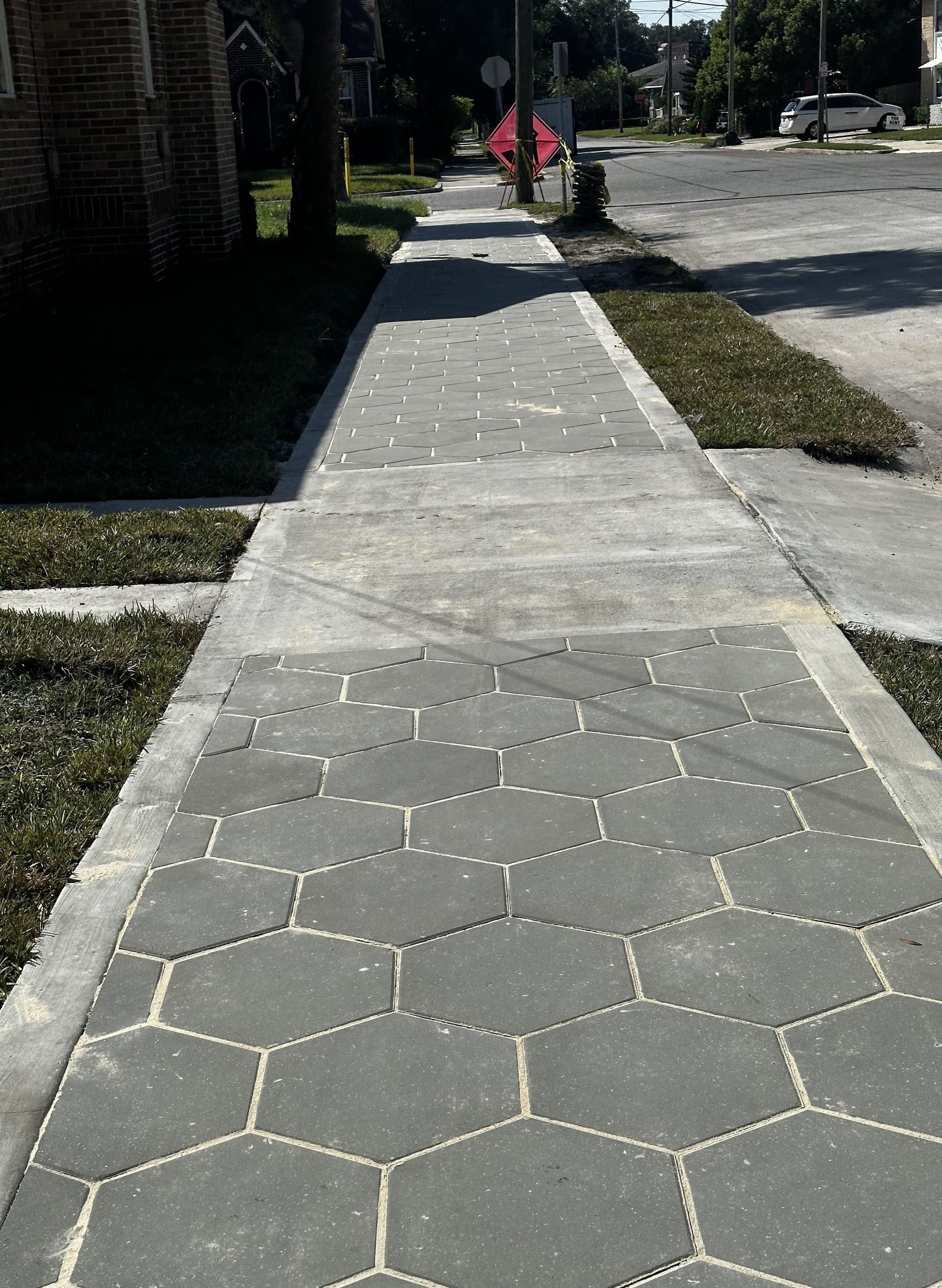 Sunny sidewalk with hexagonal paving stones and a few people in the distance near a street.
