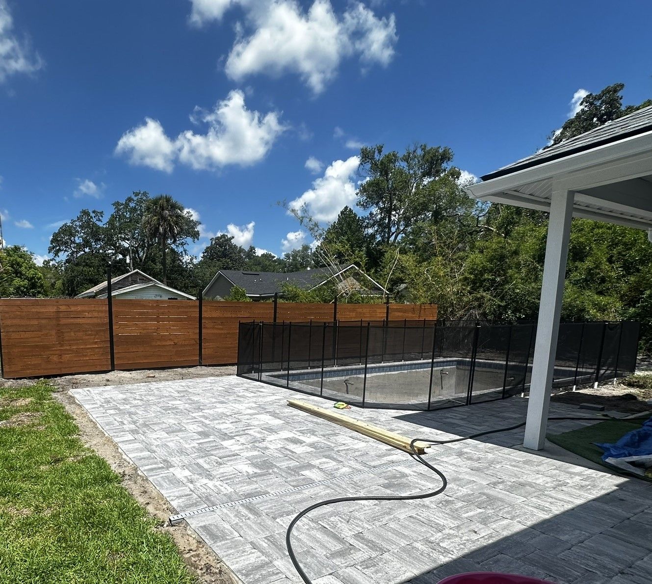 Backyard patio with gray pavers, black fence, wood privacy fence, and blue sky with clouds