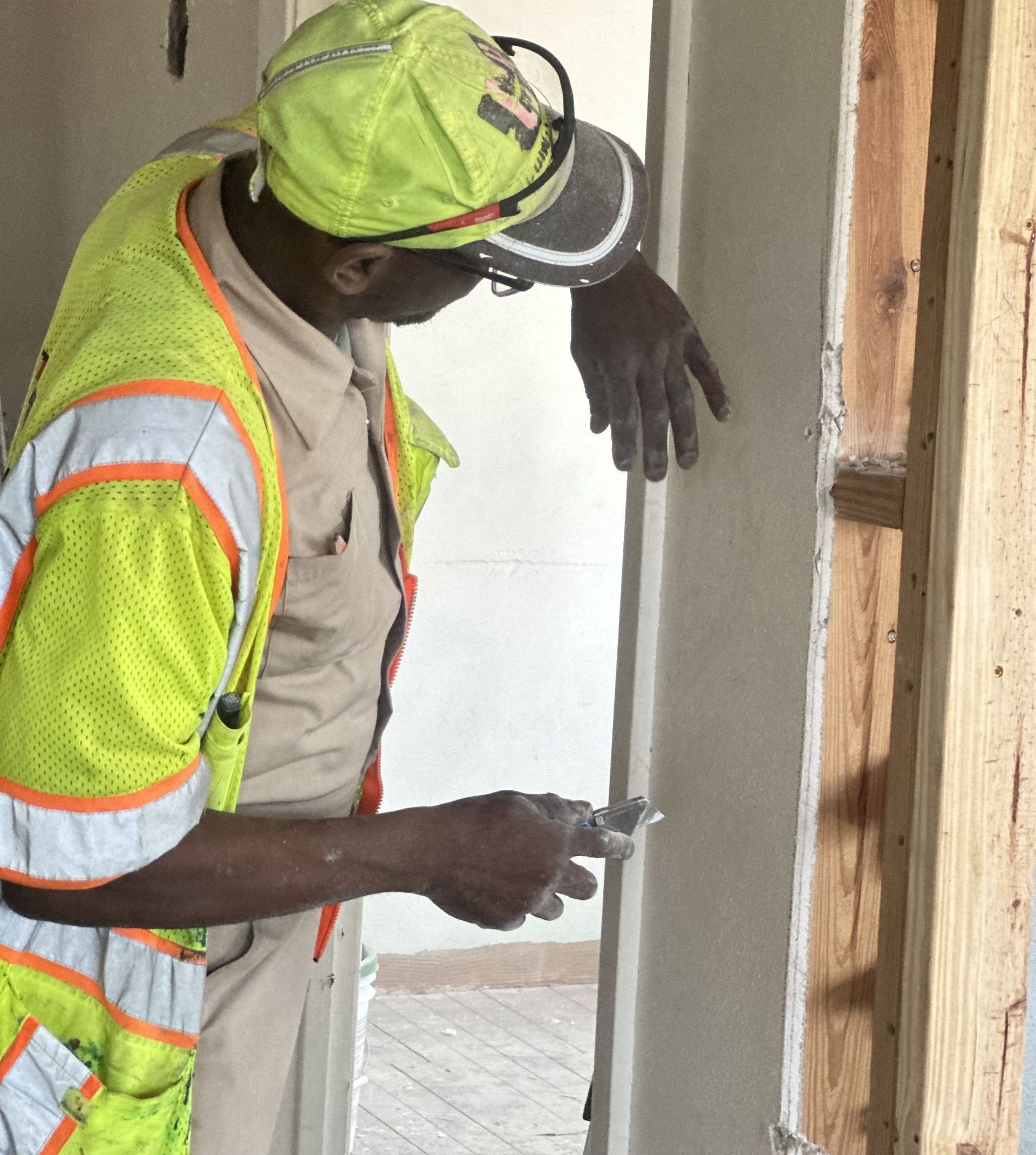 A man wearing a yellow hat is working on drywall.