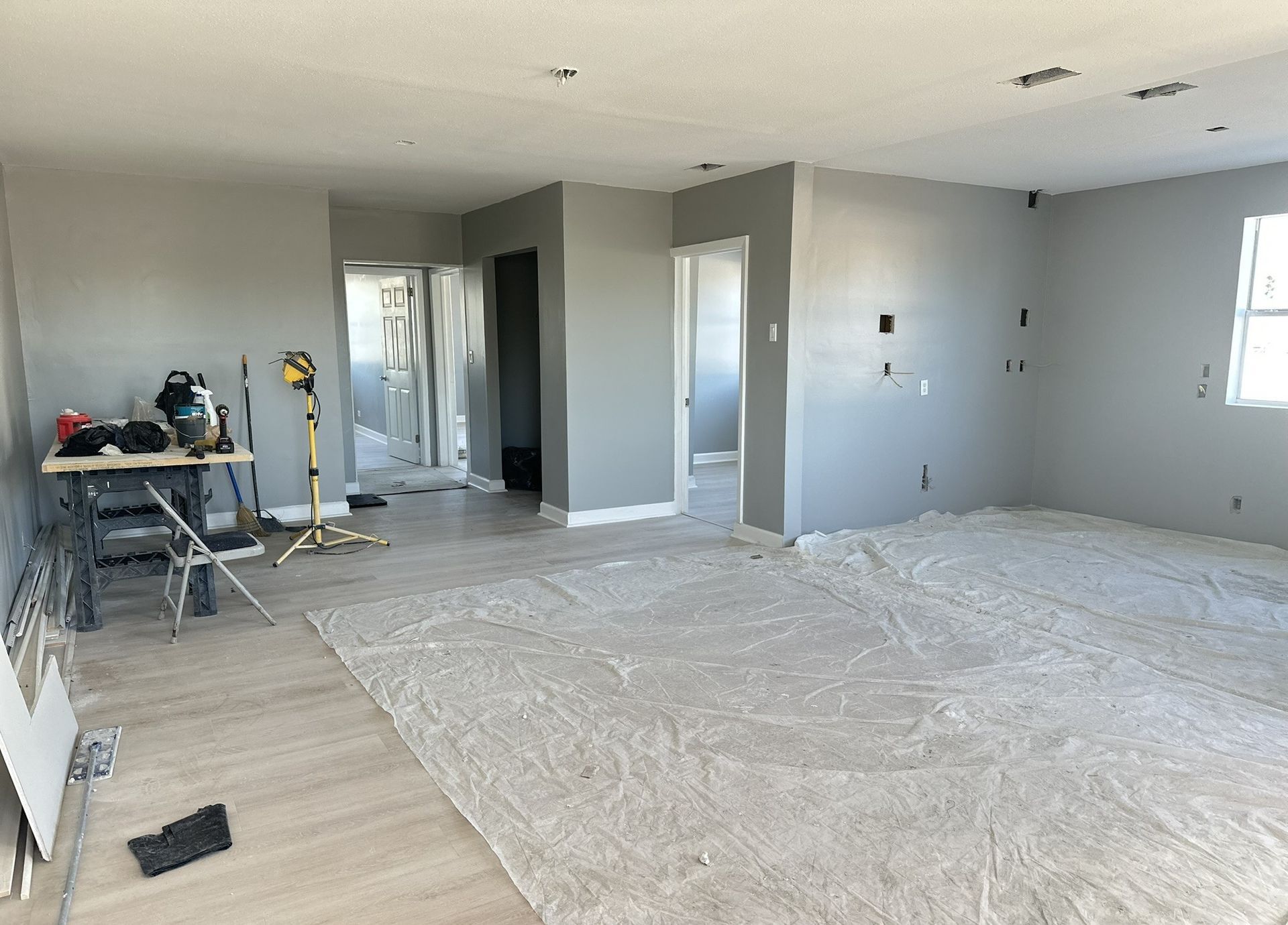 Empty living room under renovation with plastic-covered floor, gray walls, and tools near the left wall