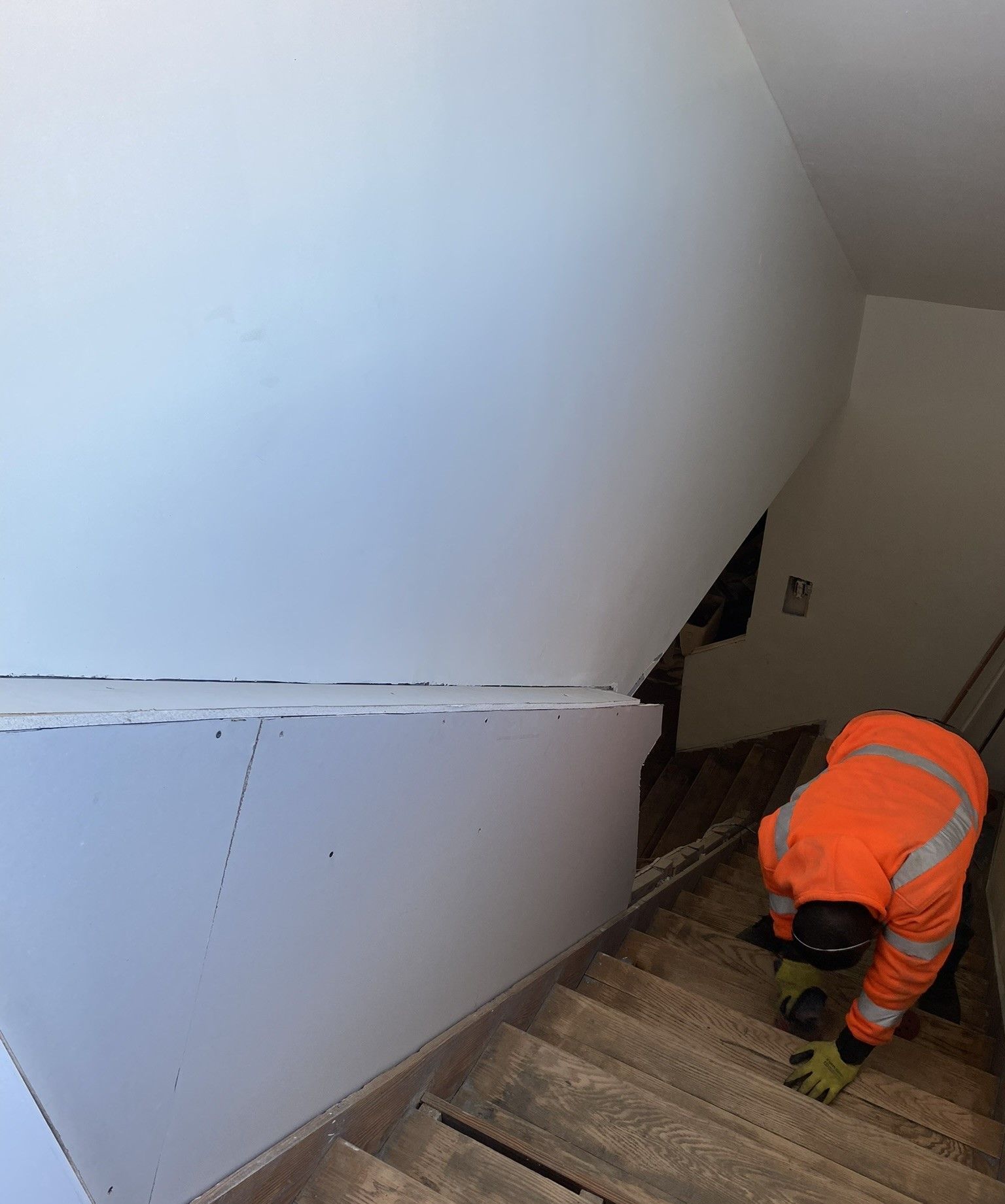 A man in an orange jacket is working on a set of stairs remodel.