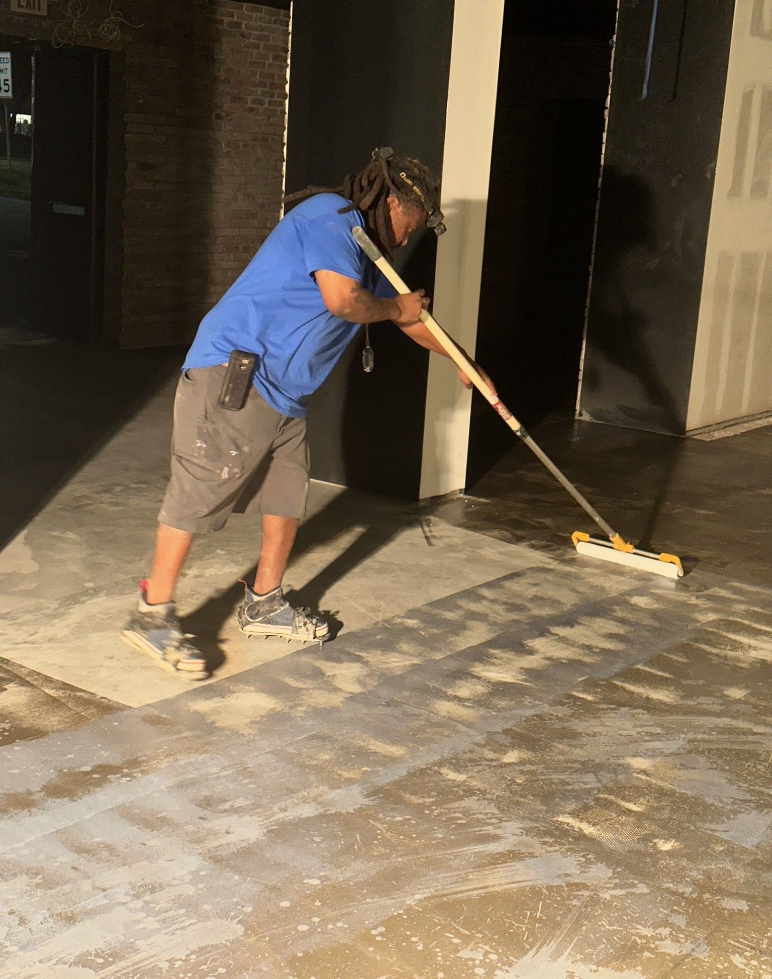 Person in blue shirt mopping a floor in a dim indoor space