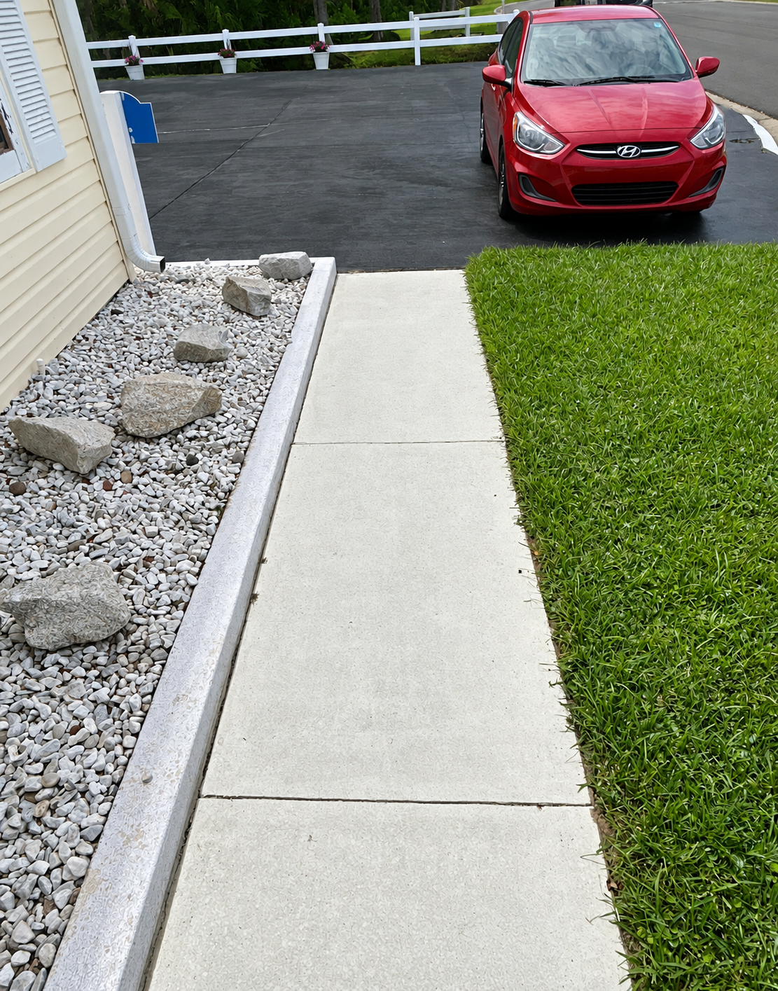 Concrete walkway beside gravel and grass, leading to a driveway with a red car parked ahead.