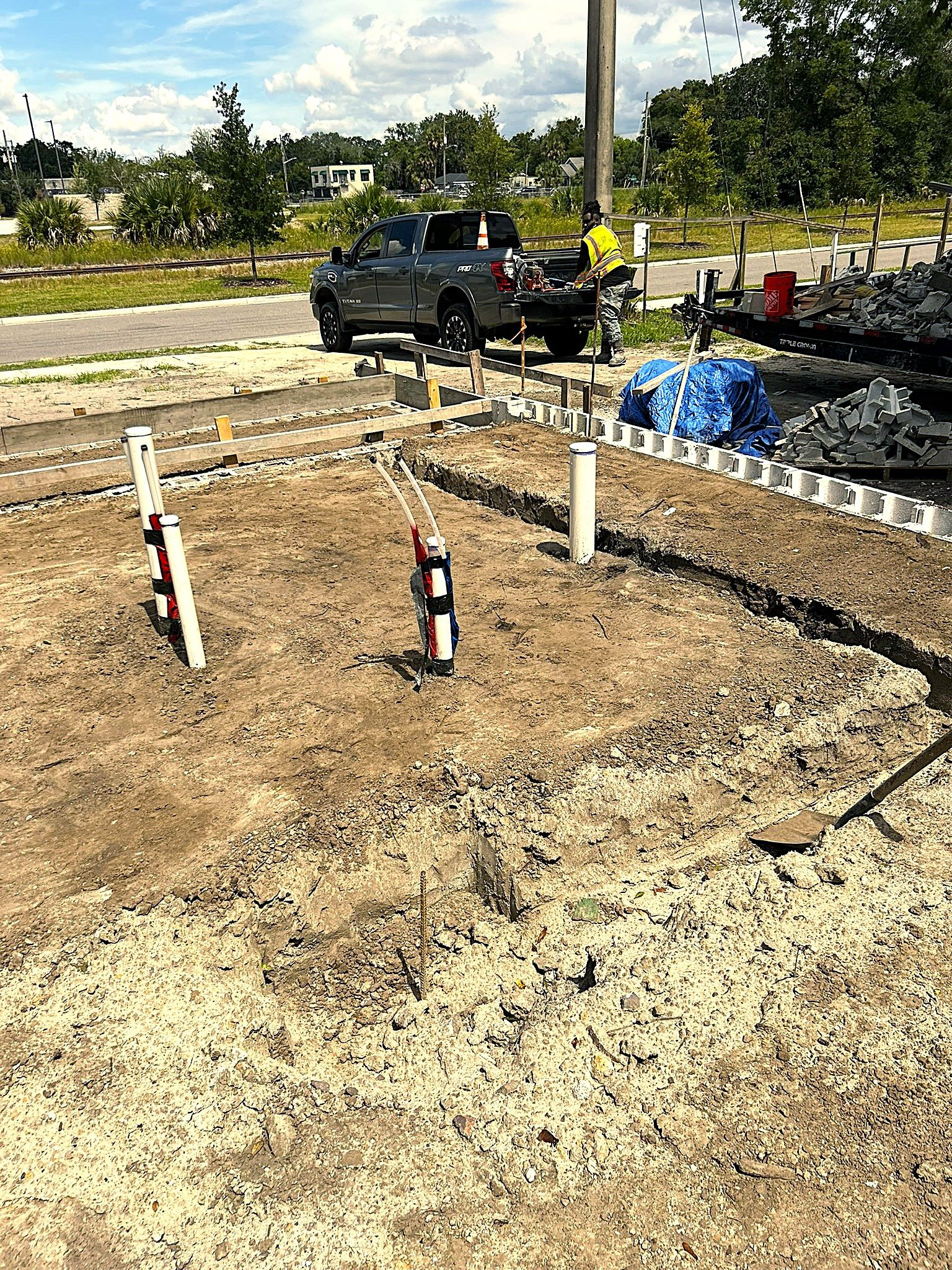 Stem wall foundation with fresh dirt, white barriers, and a black pickup truck near a roadway