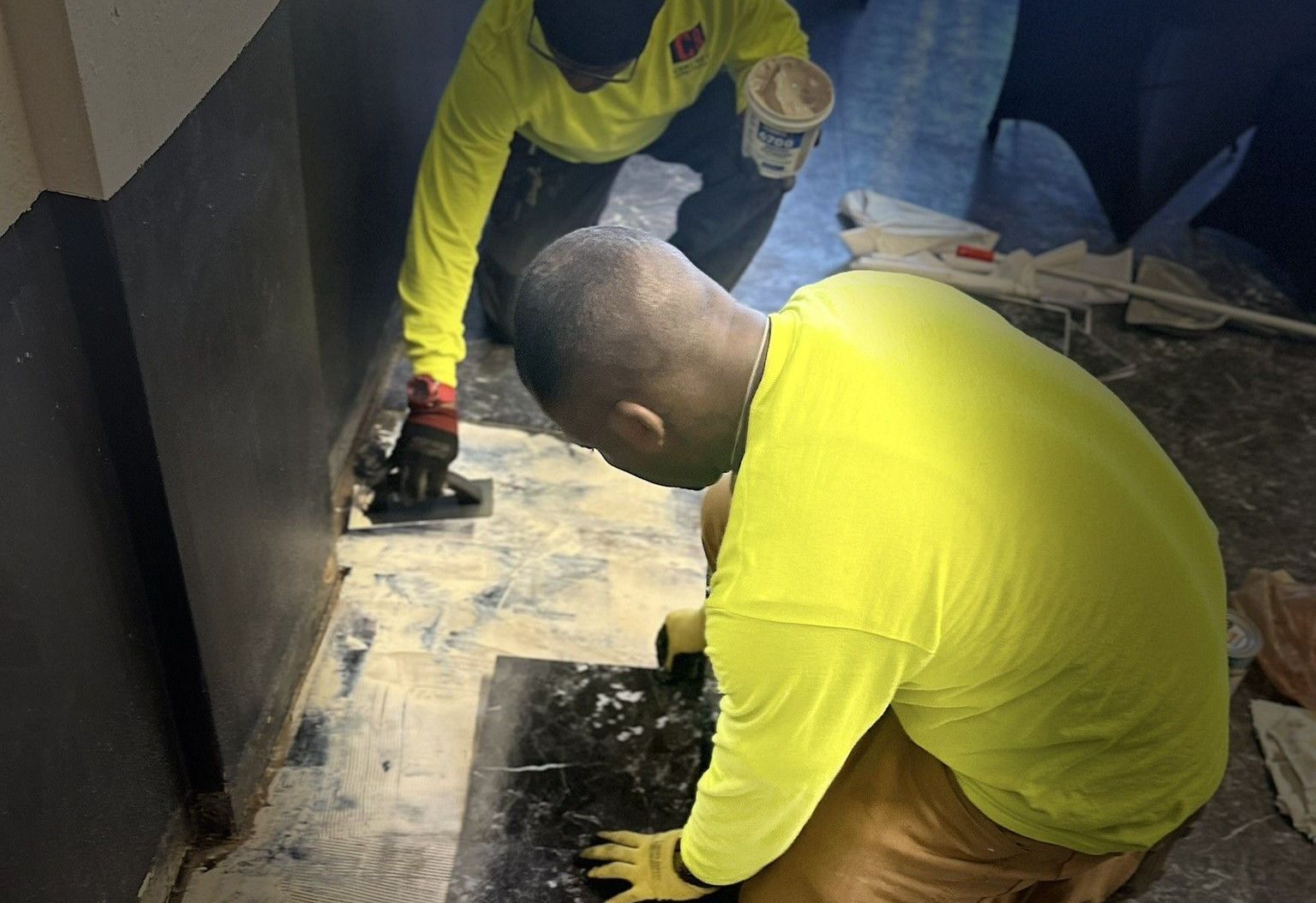 Two men are working on a floor in a room.