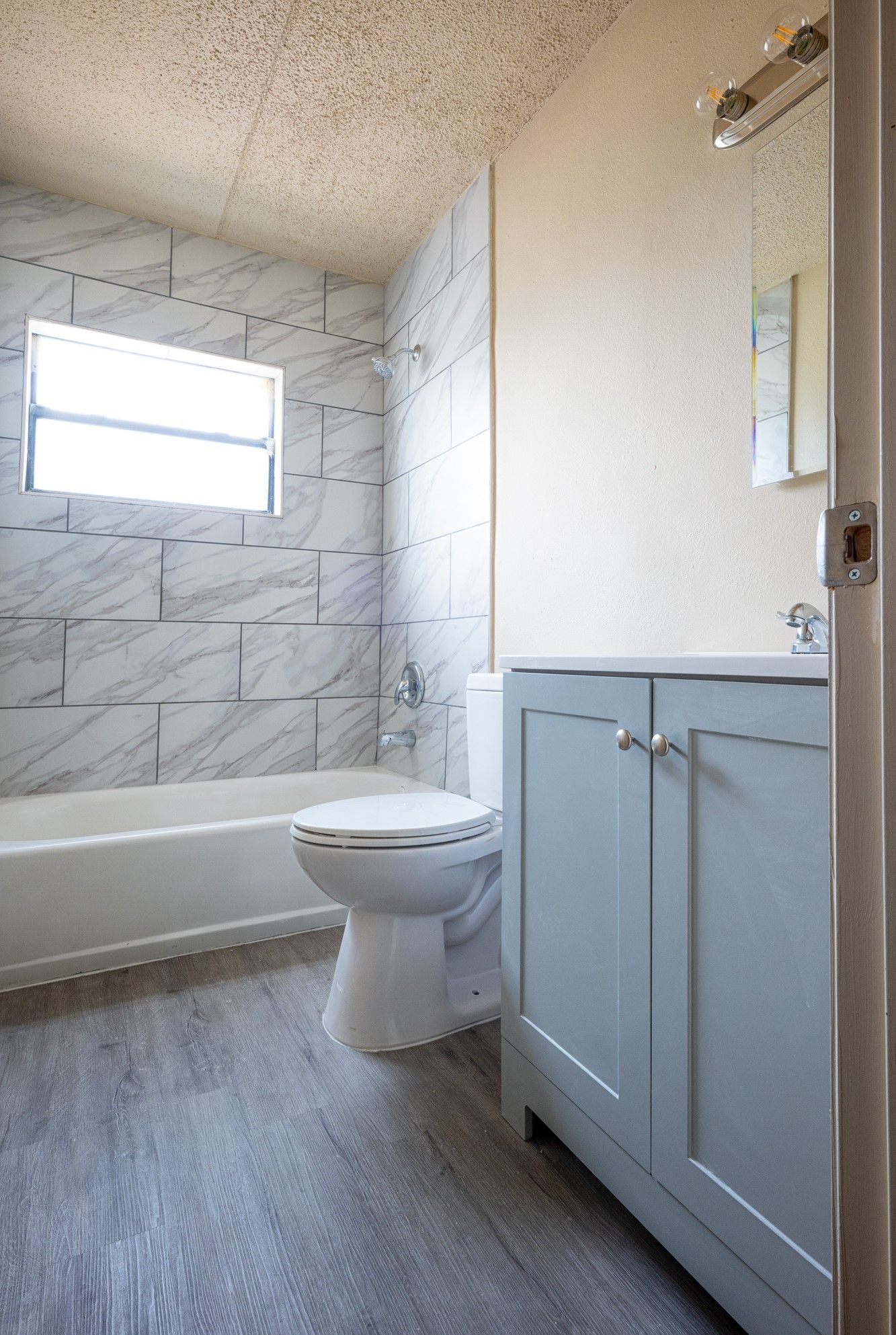Small bathroom remodel with bathtub, toilet, and blue vanity beside a window.