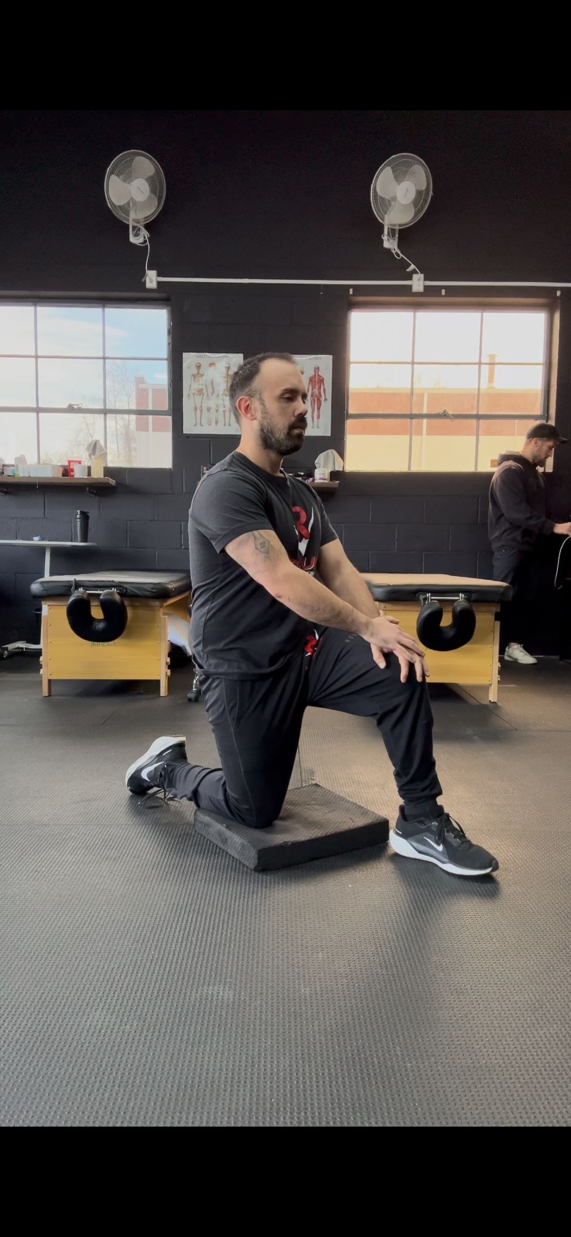 A man is kneeling on a mat in a gym.