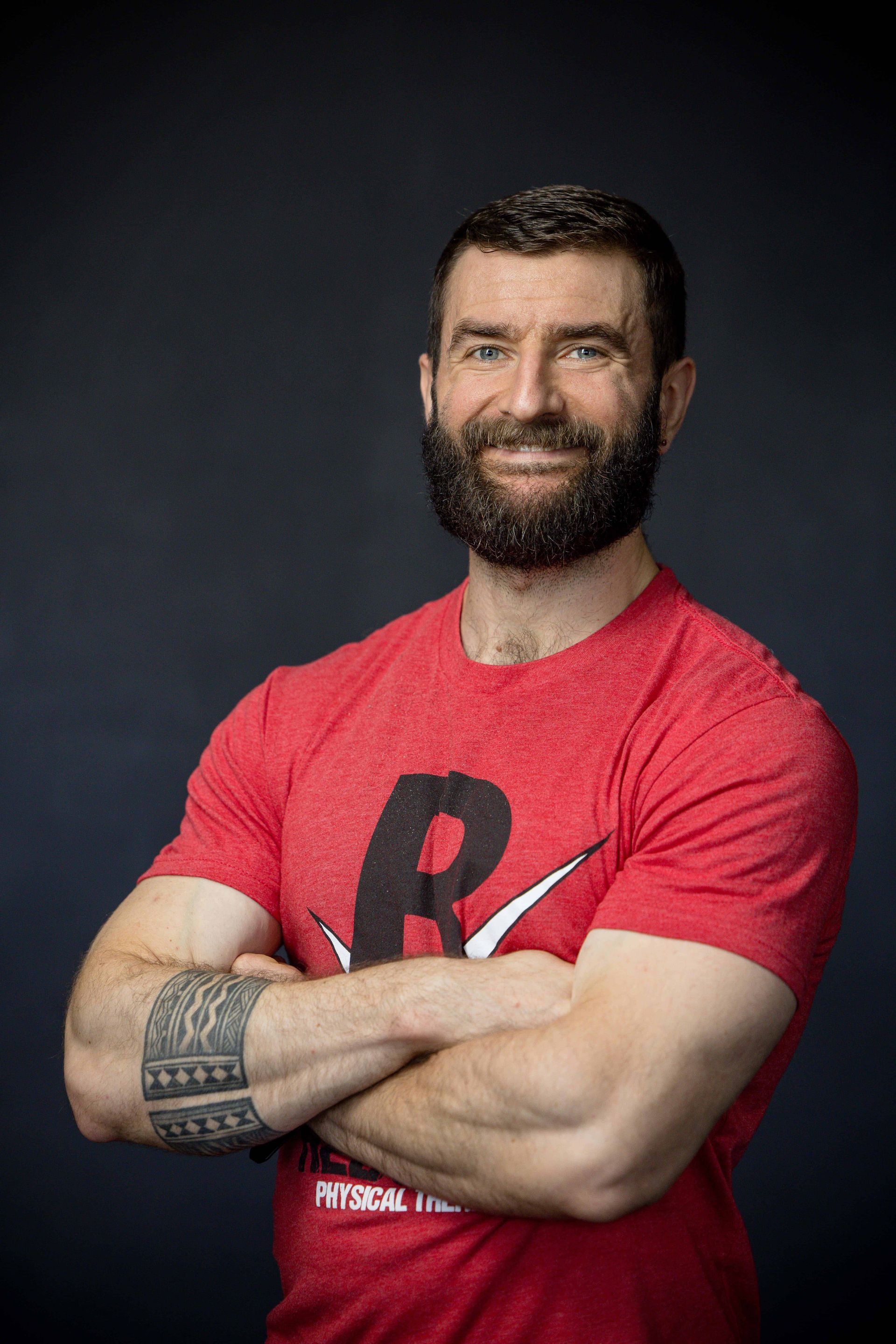 A man with a beard is standing in a gym with his arms crossed.