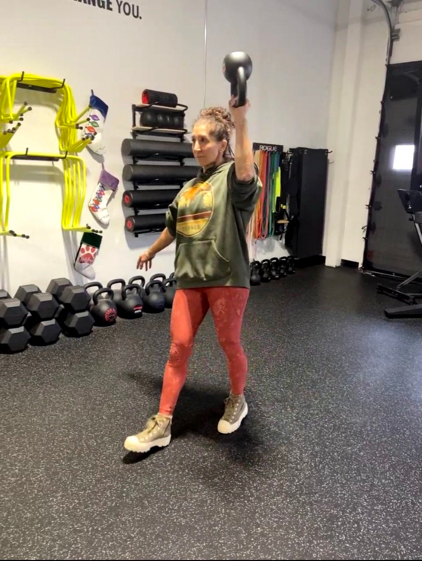 A woman is holding a kettlebell over her head in a gym.