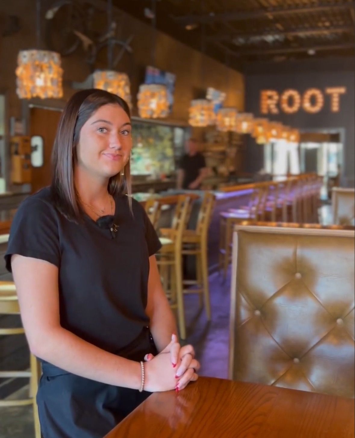 A server stands by a table in a restaurant with a bar in the background featuring illuminated