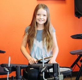 Smiling child playing electronic drums in front of an orange wall