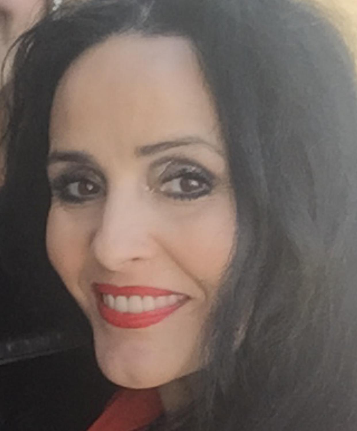 Close-up portrait of a smiling person with dark hair, red lipstick, and smoky eye makeup