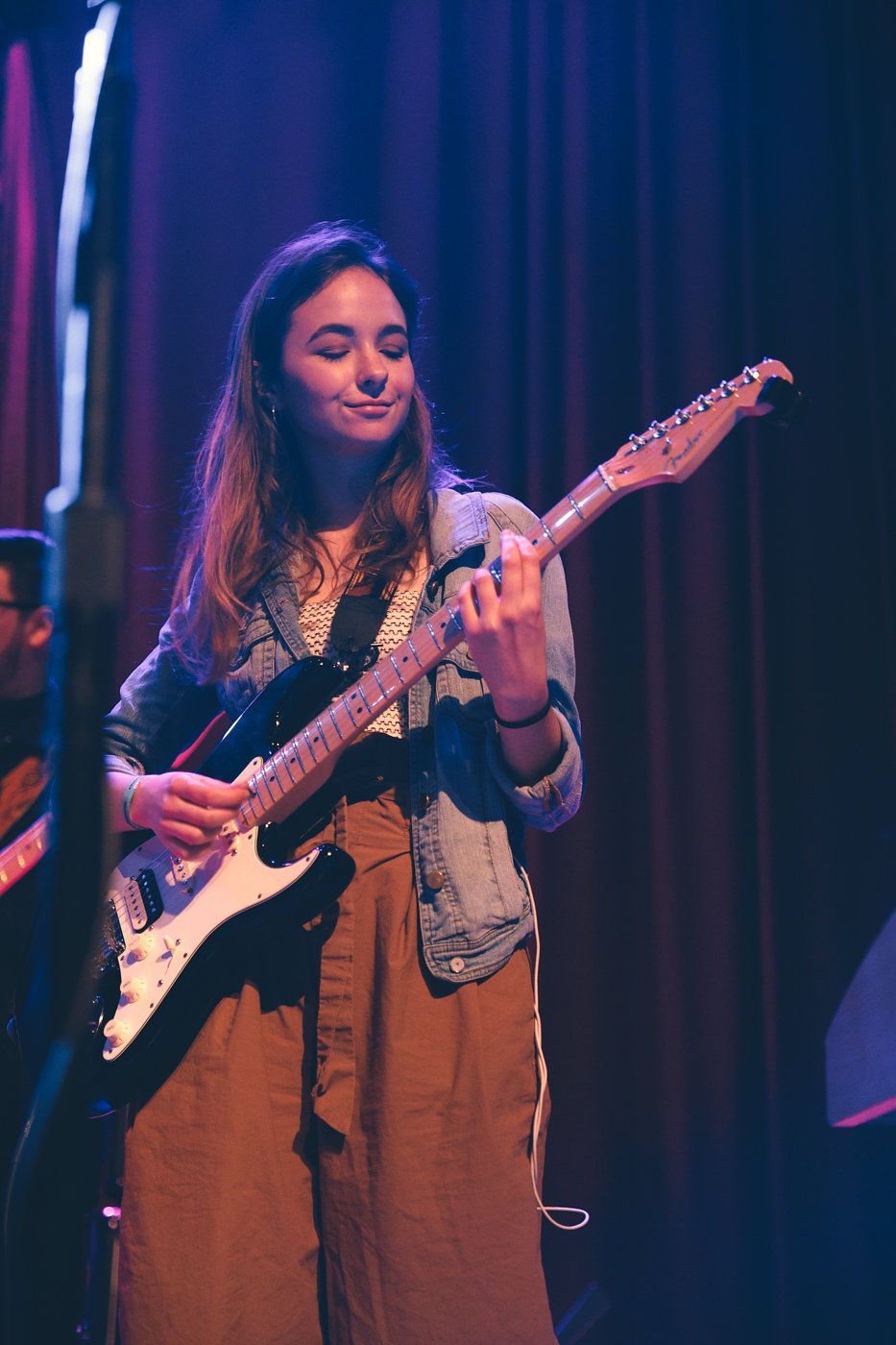Musician playing electric guitar on stage under purple lighting