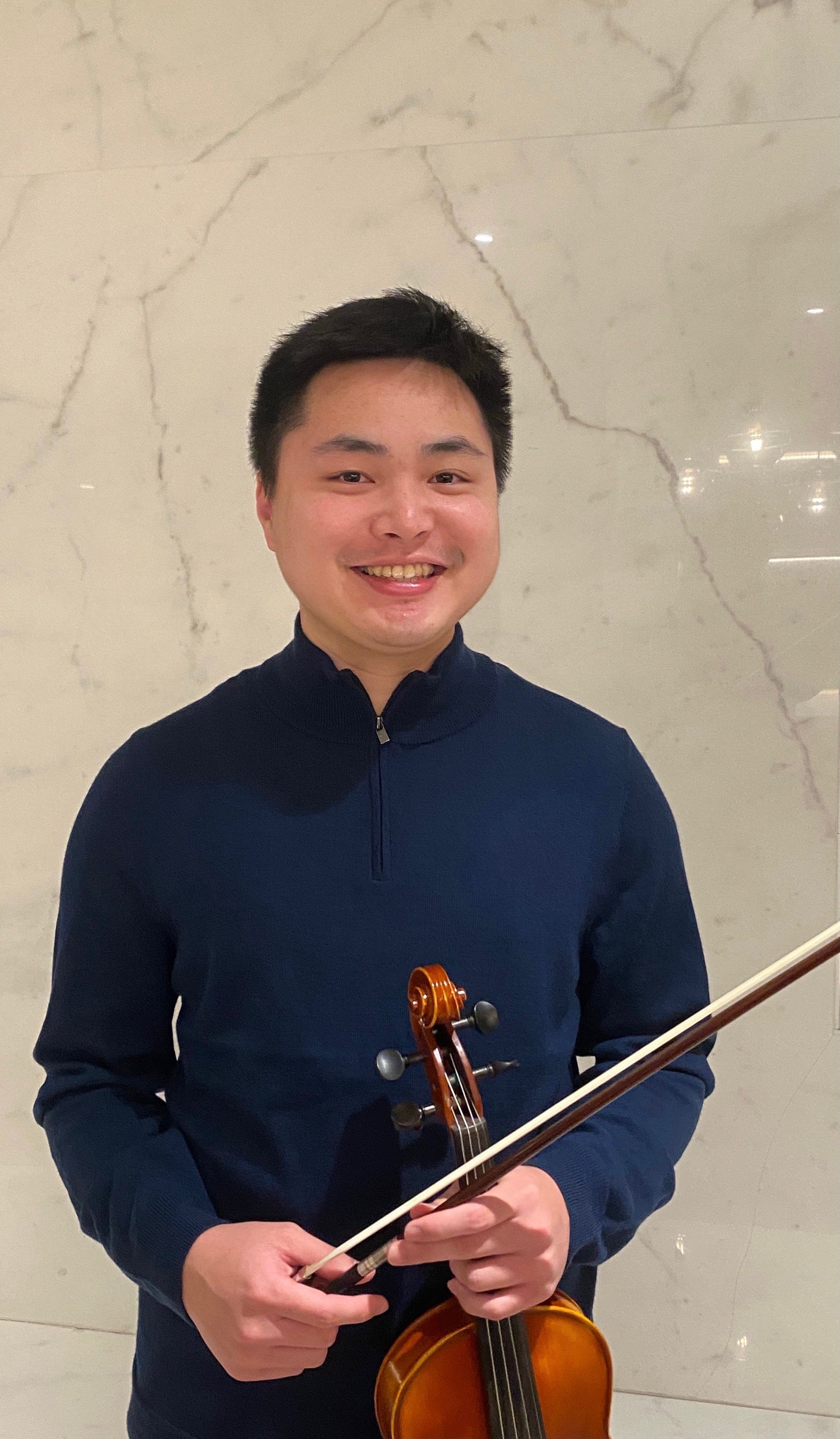 Smiling person in a navy top holding a violin and bow against a marble wall.