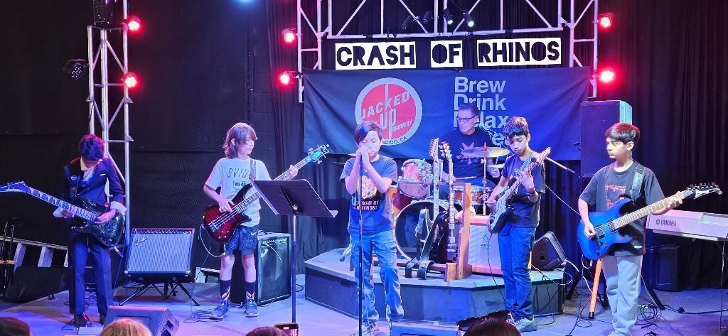 Band performing on a lit stage under a “Crash of Rhinos” banner.
