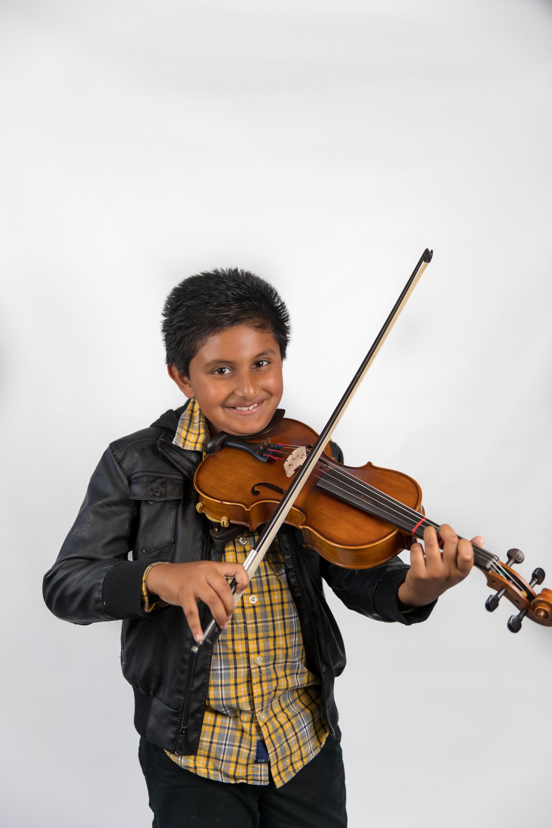 Young musician smiling while playing a violin against a plain white background