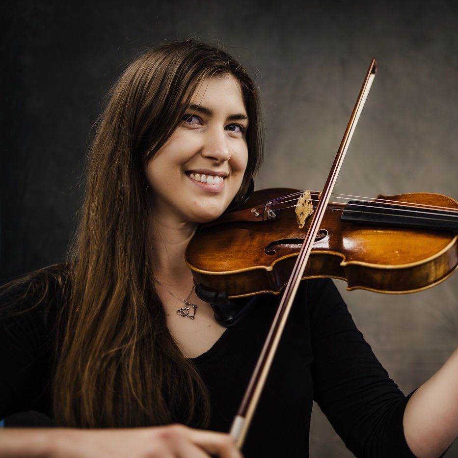 Smiling musician playing violin against a dark studio backdrop