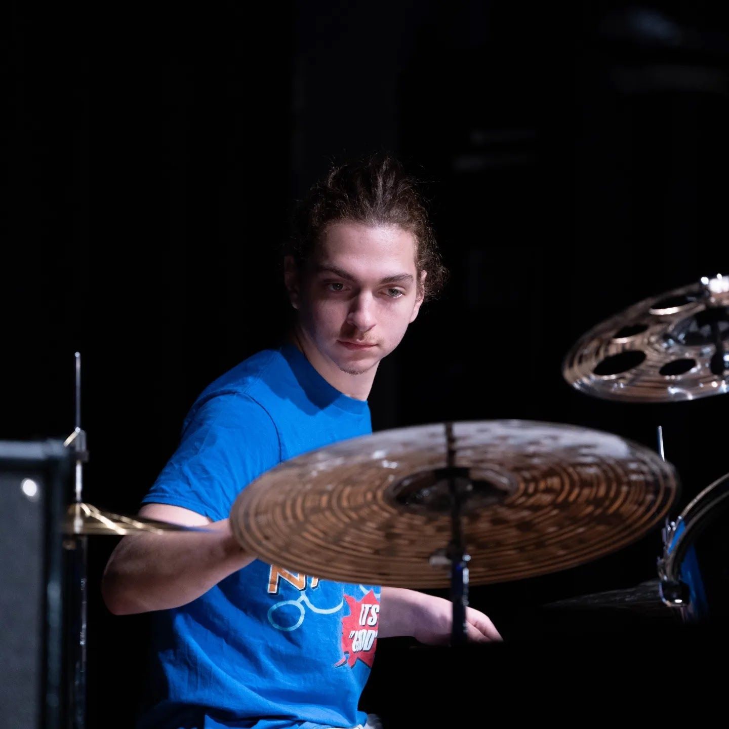 Drummer in a blue shirt playing cymbals on a dark stage