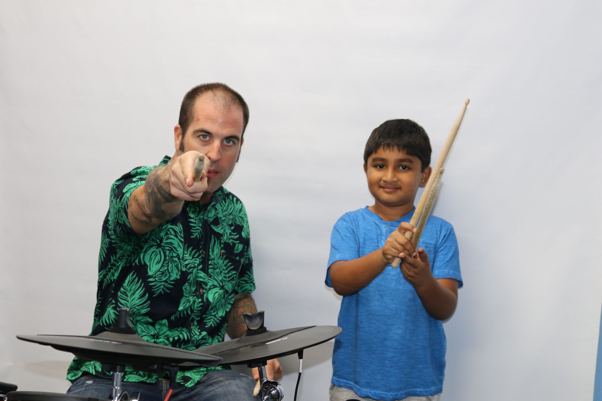 Two people posing; one points at the camera while the other holds a drumstick-like stick.