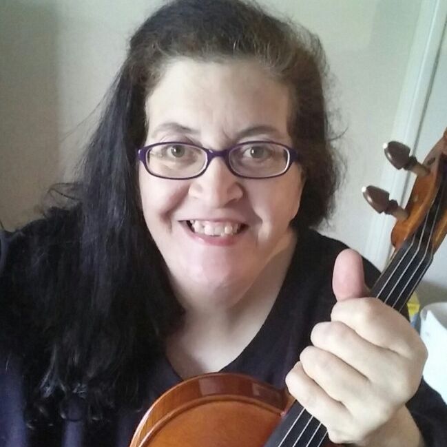 Woman smiling with a violin, wearing glasses and a black top, against a light background