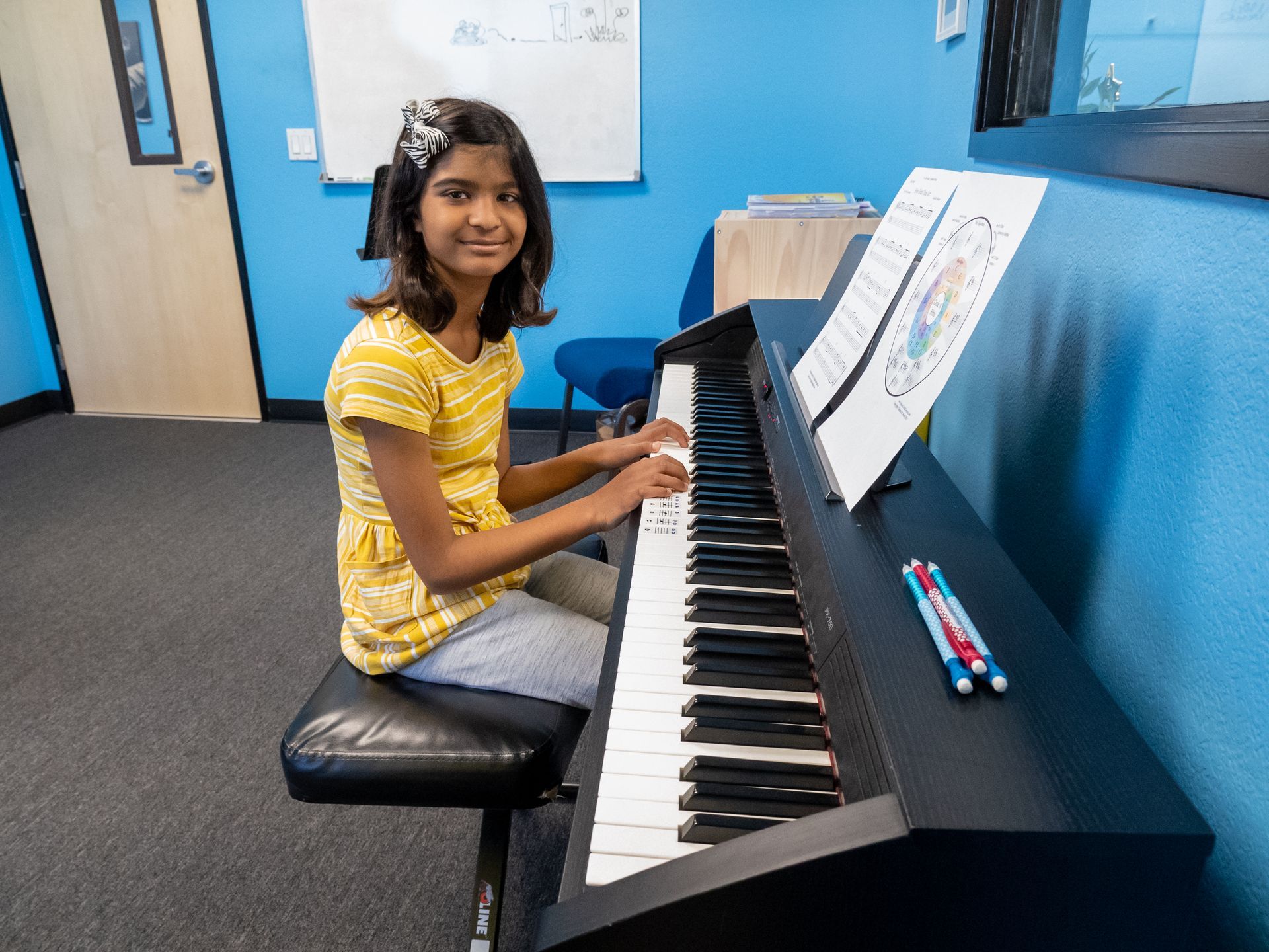 Person playing a digital piano in a music room, with sheet music on the stand and a blue wall behind.
