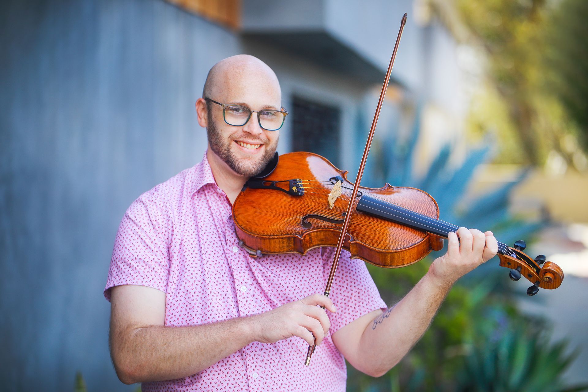 Man smiling while playing a violin outdoors against a soft blue background