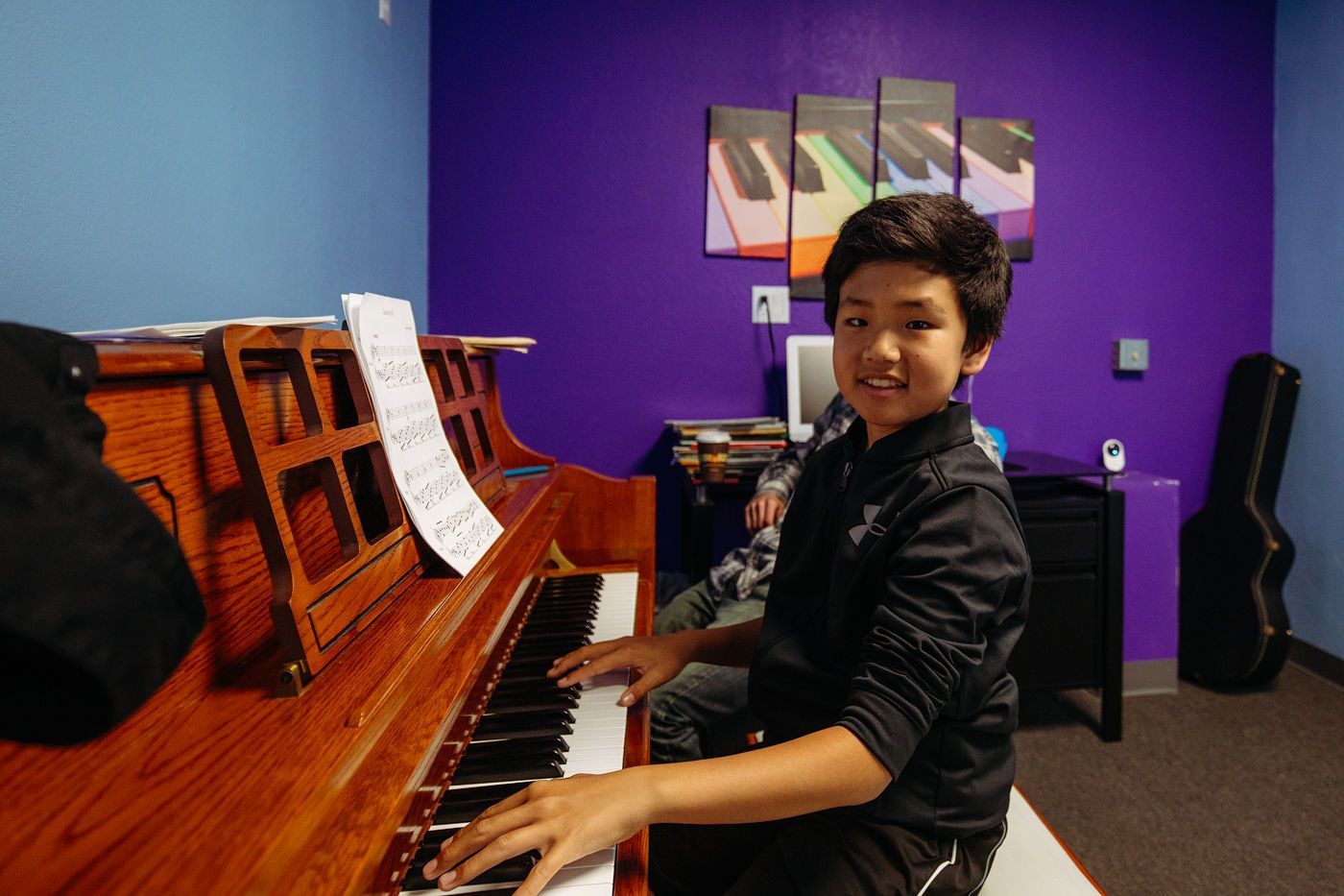 Person smiling while playing an upright piano in a purple music room
