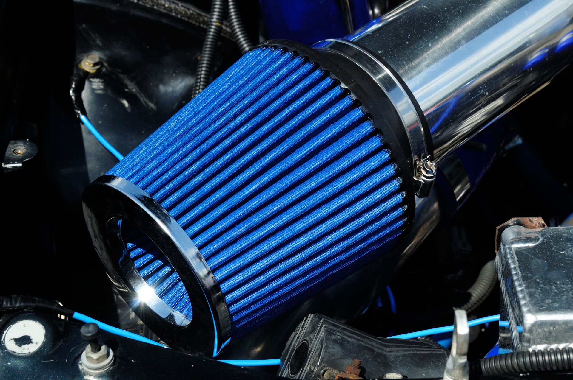 A bright blue conical performance air filter attached to a metallic intake pipe inside a car engine bay.
