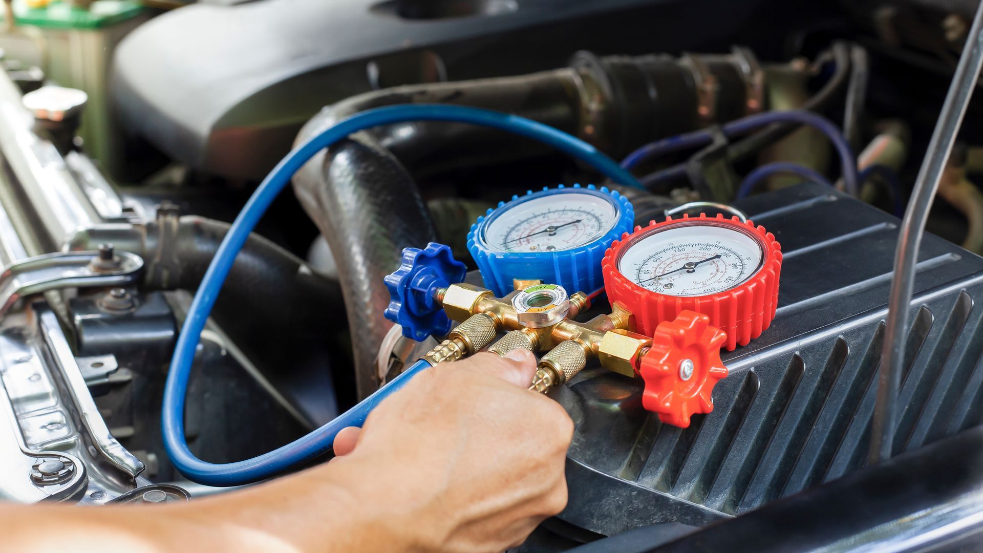 A person uses a blue and red manifold gauge set to check or service an automotive air conditioning system.